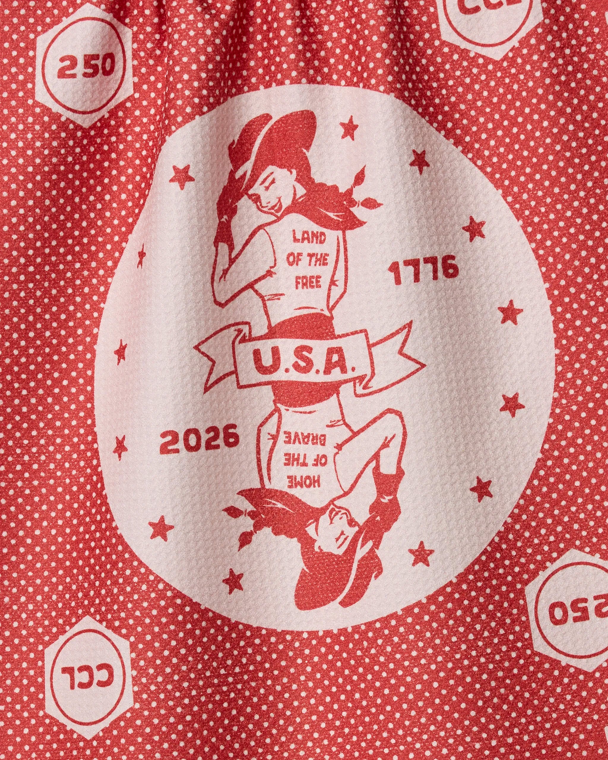 The Geometry USA Cowgirl kitchen tea towel features a red and white circular cowgirl design, "U.S.A." banner, "LAND OF THE FREE," "HOME OF THE BRAVE," and the years 1776 and 2026. Made from recycled materials.