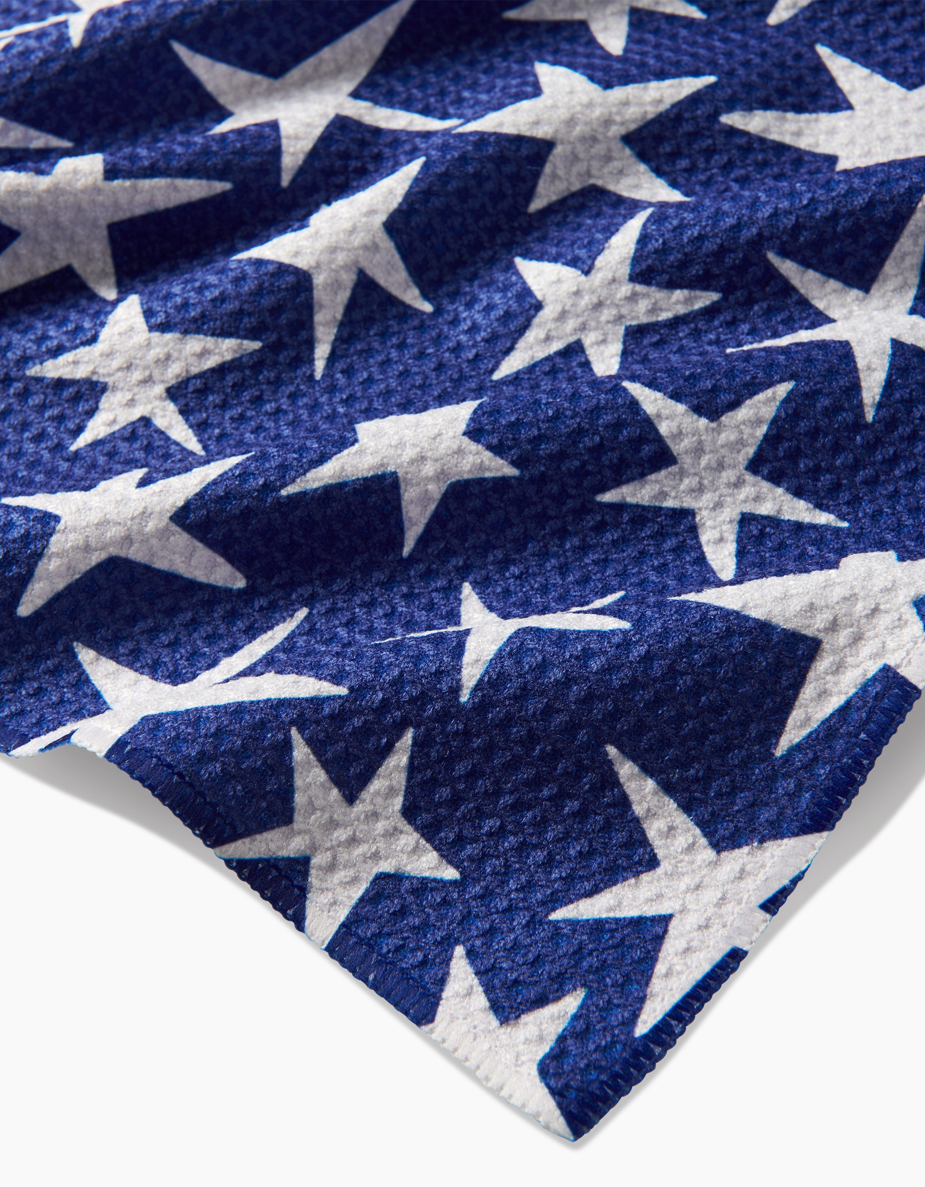 A close-up of the Mindfulnice USA Stars Tea Towel shows its blue Geoweave fabric with large, irregularly placed white stars, giving the towel a unique textured look.