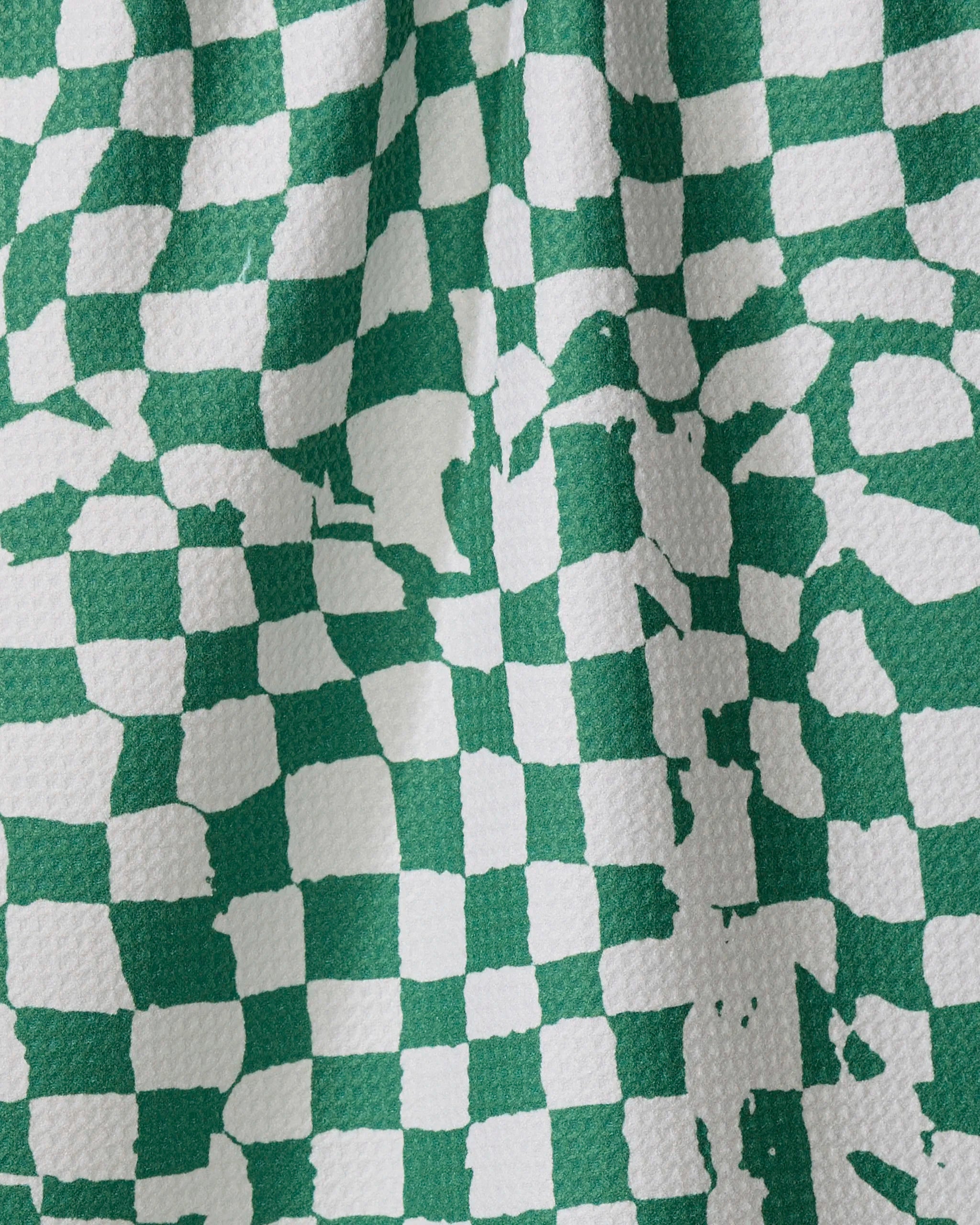 Geometry’s Verdant dish towel features a green and white checkered design with a wavy, textured surface. Some pattern areas appear abstract or faded, creating an irregular look.