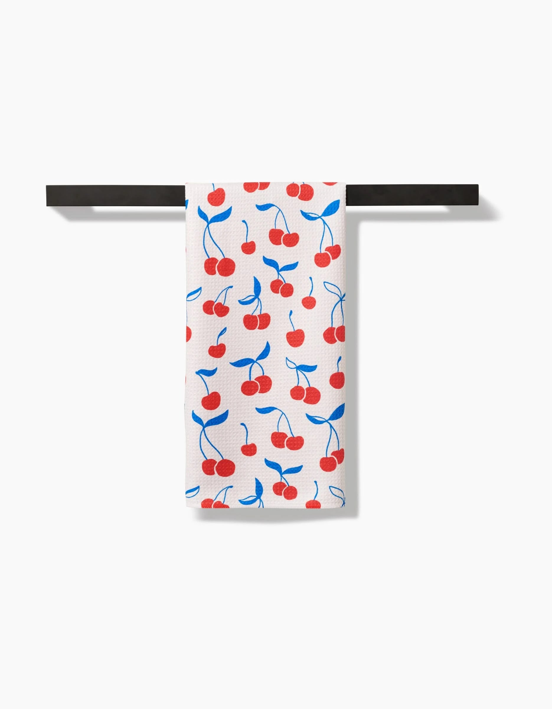 The Very Cherry tea towel by Kayla Ann, crafted from Geoweave fabric, displays a red cherry and blue stem design and hangs neatly over a black bar on a plain white background.
