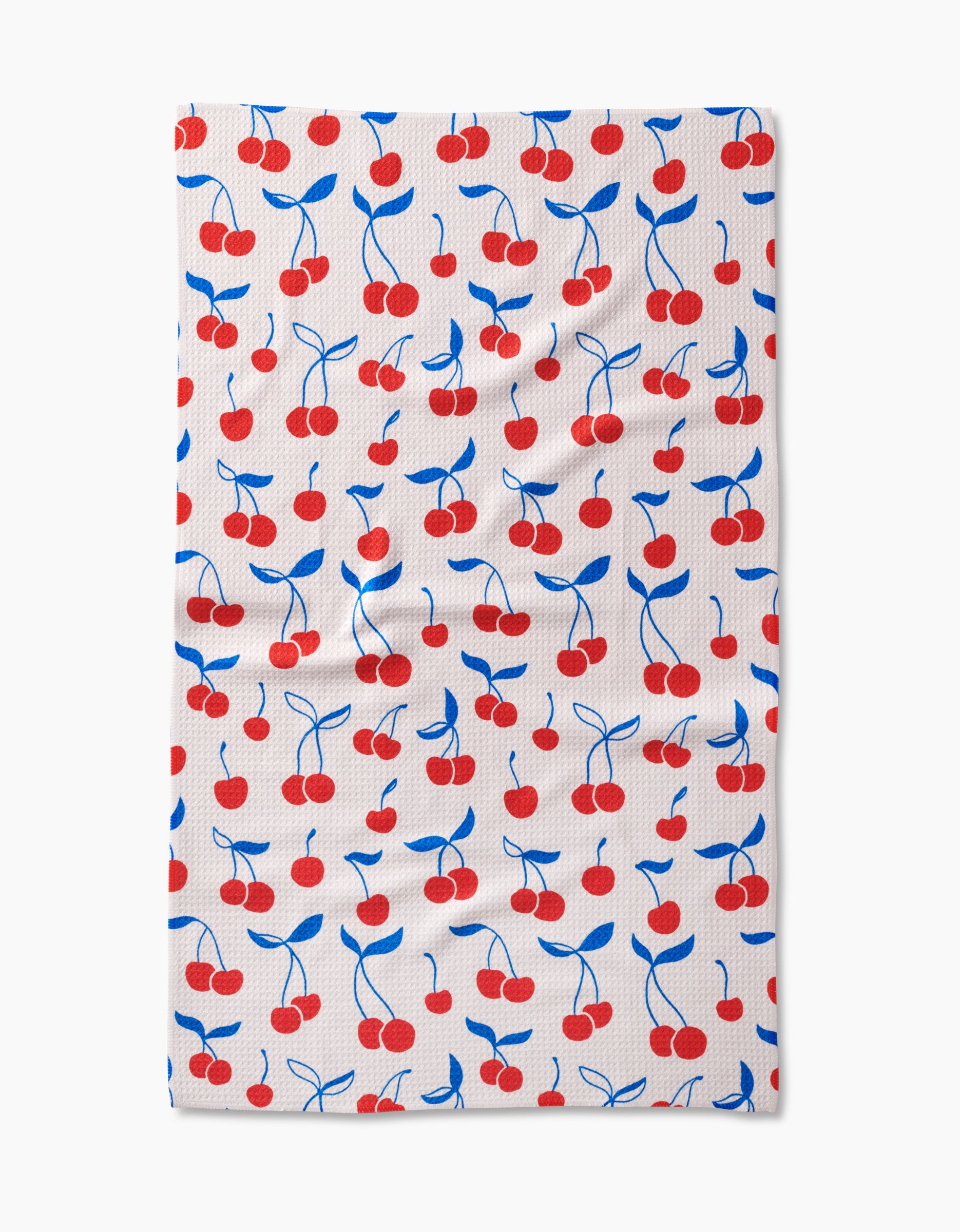 The Kayla Ann Very Cherry tea towel features a rectangular white design with a repeating pattern of red cherries and blue stems/leaves. Made from Geoweave fabric, it has small textured dots and occasional visible wrinkles.