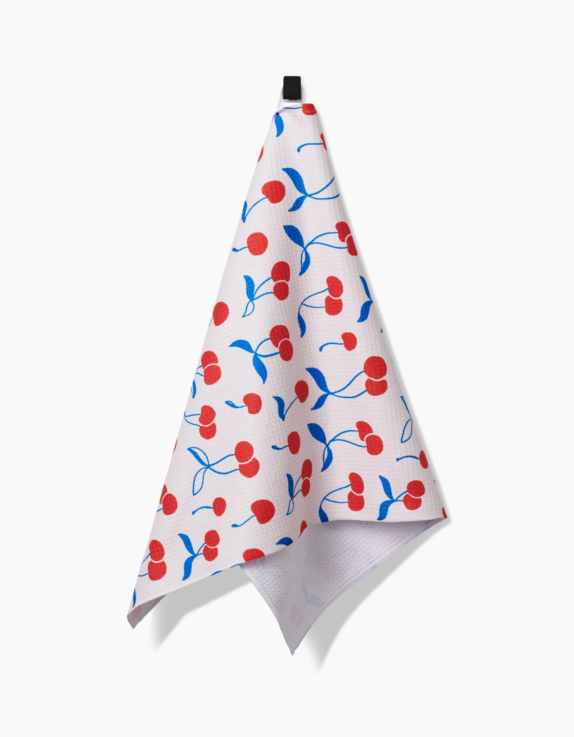 The Kayla Ann Very Cherry tea towel, made from Geoweave fabric and featuring red cherries with blue leaves, hangs by a black loop against a plain white background.