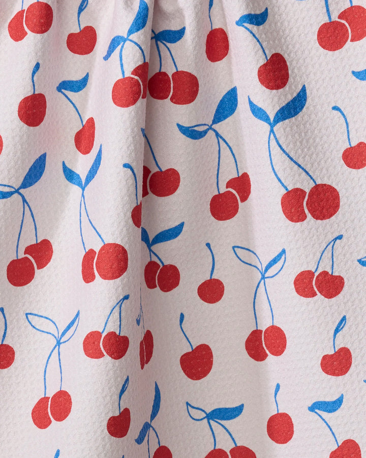 Close-up of the Kayla Ann "Very Cherry" white kitchen tea towel, featuring a textured design with red cherries, blue stems and leaves, and a gathered seam near the top.