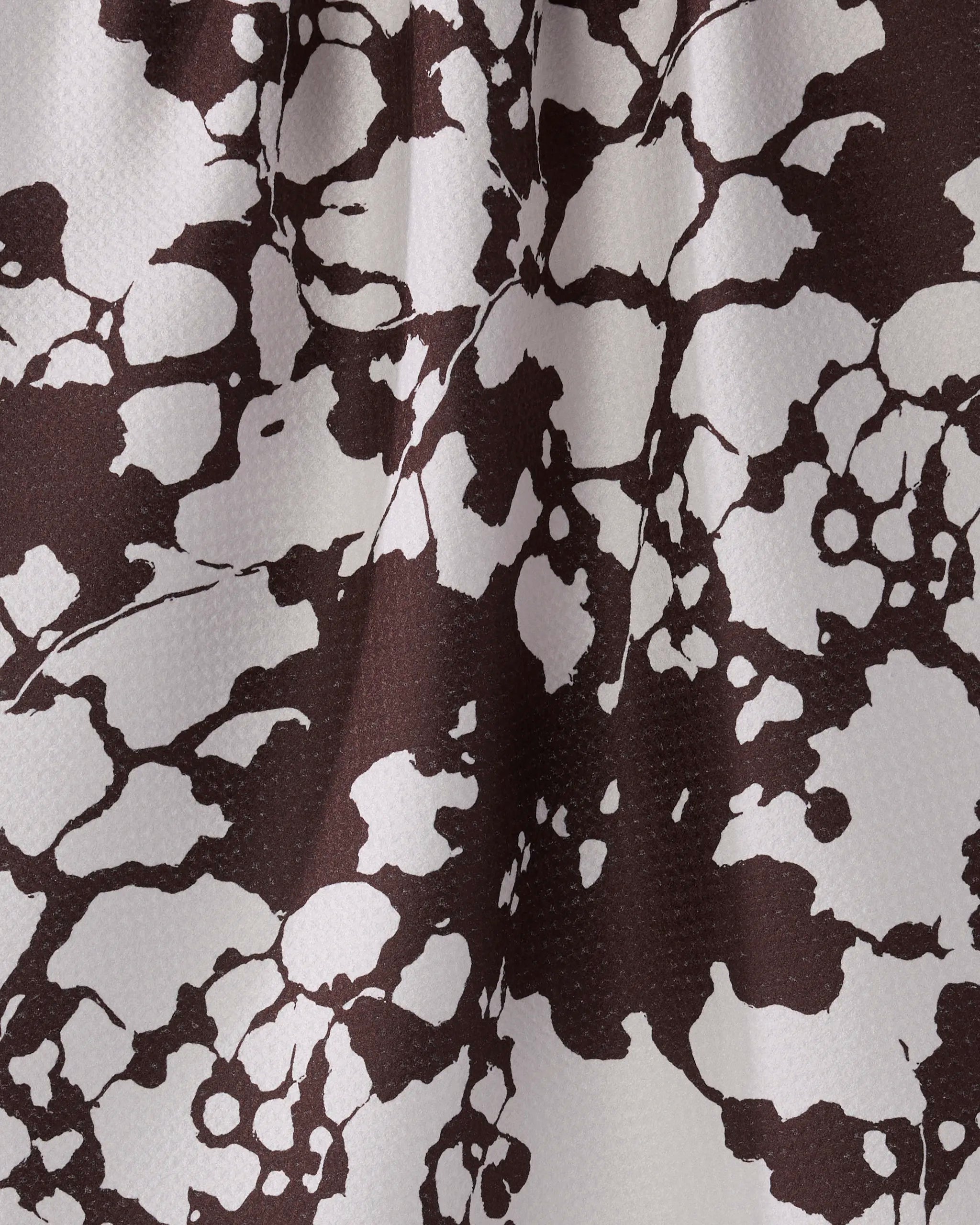 Close-up of the Geometry Vine Noir tea towel, showcasing an irregular brown and white abstract pattern with a mottled texture, enhanced by subtle folds and shadows for added depth.