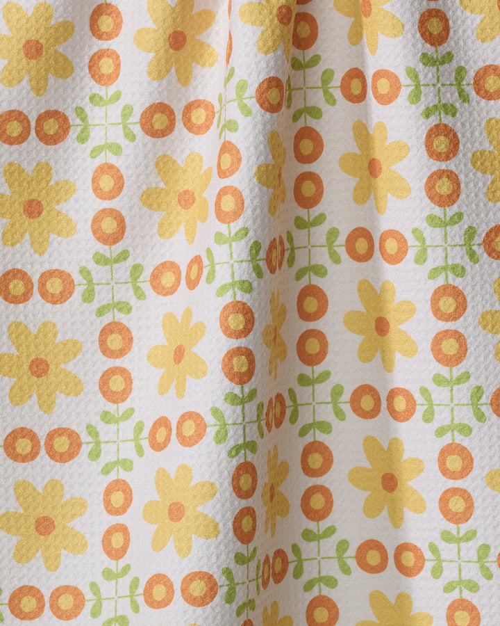 The Mindfulnice "Vintage Blooms" tea towel features yellow flowers, orange circles, and green leaves in a grid on white. Made from ultra-absorbent recycled materials, it’s an eco-friendly, stylish choice for your kitchen.