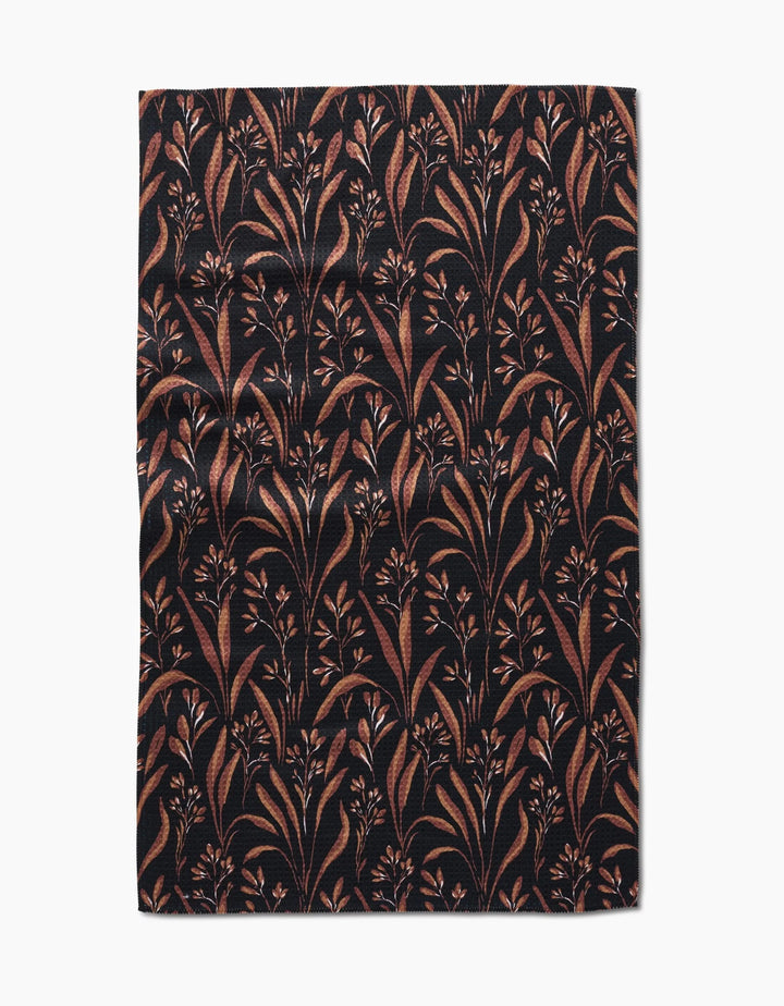 The Hufton Studio Vintage Grass Black tea towel is rectangular, made from Geoweave fabric, and features a black background with brown and tan leafy branches and small flowers, shown flat with slight wrinkles.
