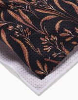 A close-up of two folded fabrics: the top is Hufton Studios Vintage Grass Black tea towel featuring a brown-beige botanical pattern, while the bottom is a textured white Geoweave waffle weave fabric.