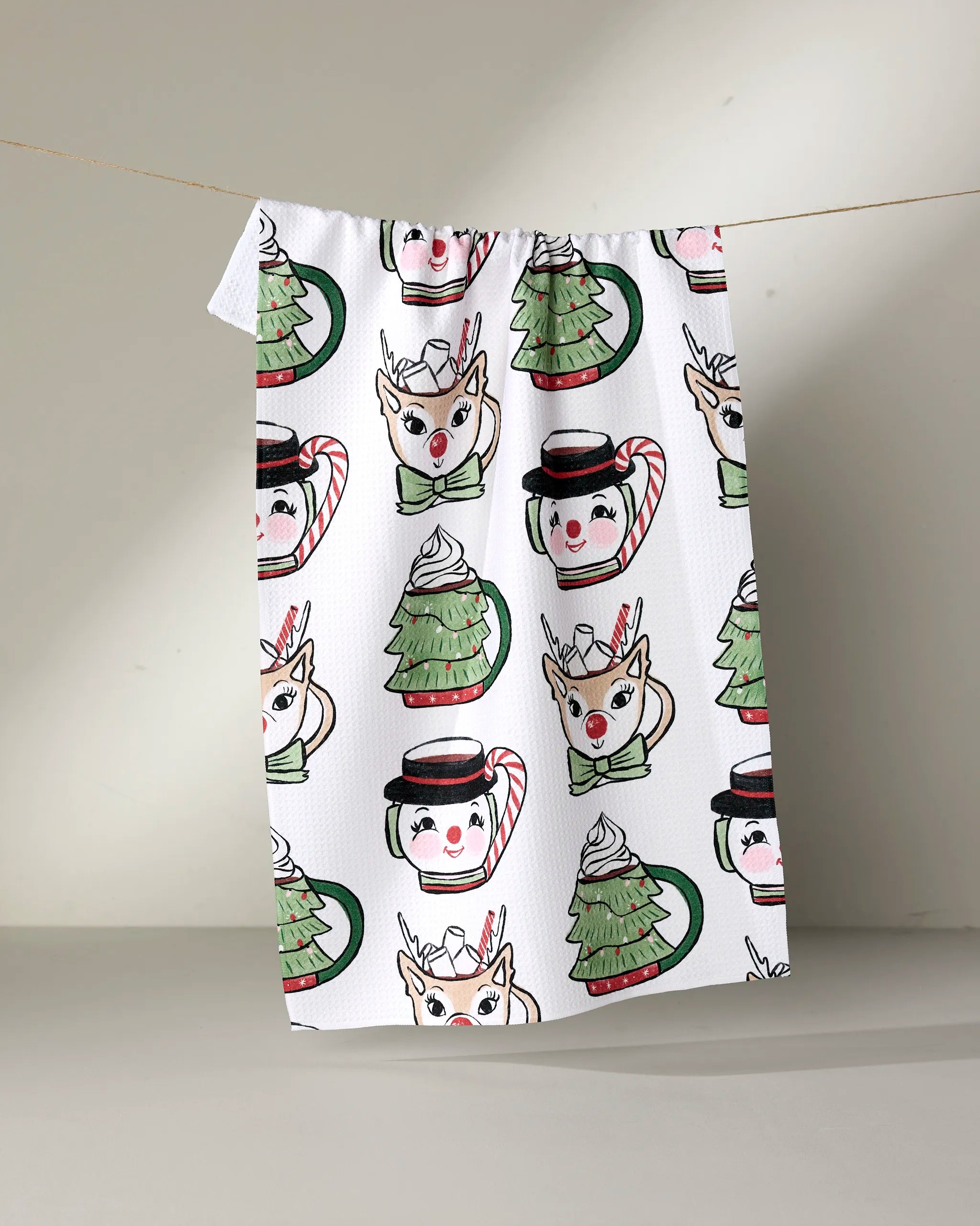 Brighten your kitchen this season with the Louise Pretzel Vintage Mugs tea towel, featuring festive reindeer faces, Christmas trees, mugs with snowman faces, and candy canes in cheerful red, green, and black tones.
