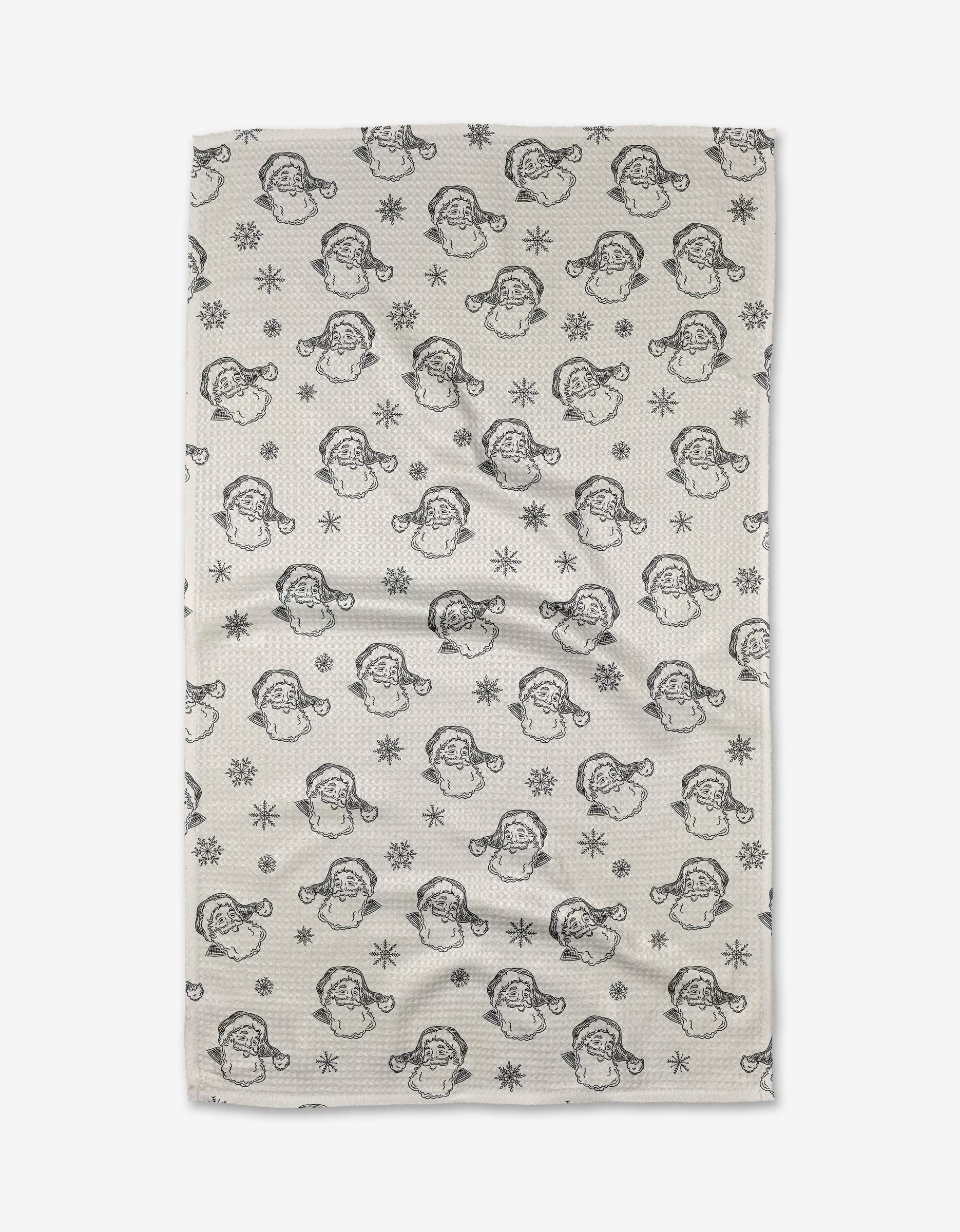 The Aubrey Fairchild Vintage Santa tea towel features a cream background with black line art of Santa faces and snowflakes. Made from recycled materials, this ultra-absorbent towel adds festive charm to any kitchen. Displayed flat with subtle wrinkles.