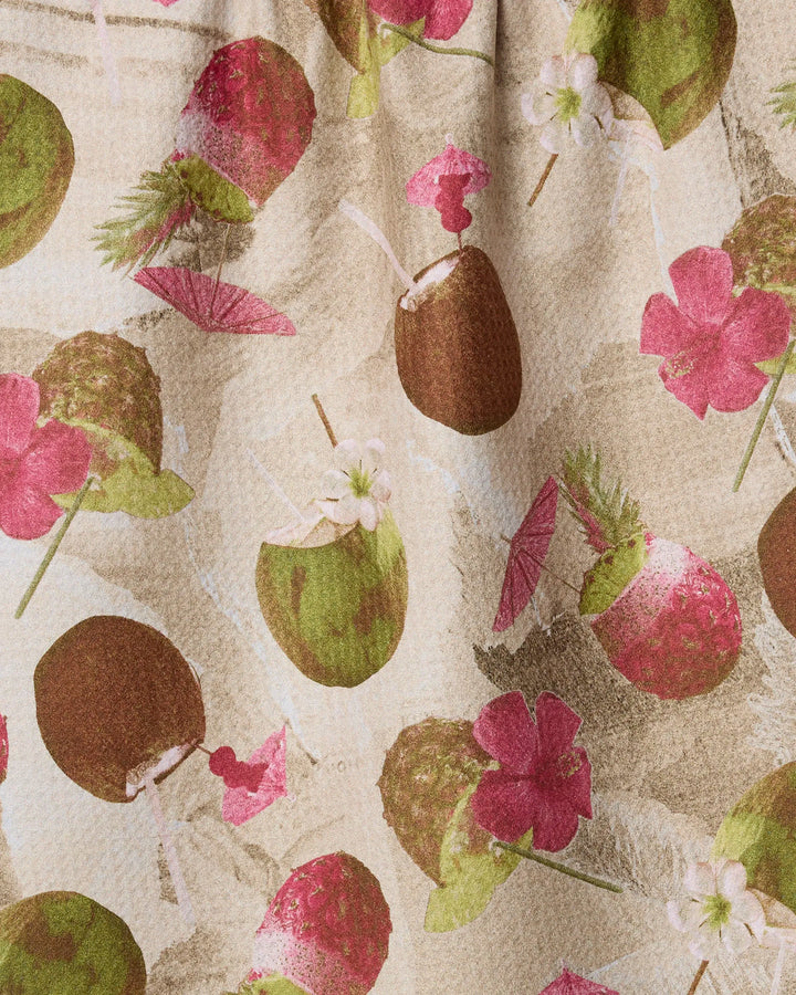 Brighten up your kitchen with Geometry’s Vintage Tropi Drinks tea towel, featuring coconuts, pink flowers, green leaves, and paper drink umbrellas on a light beige background.