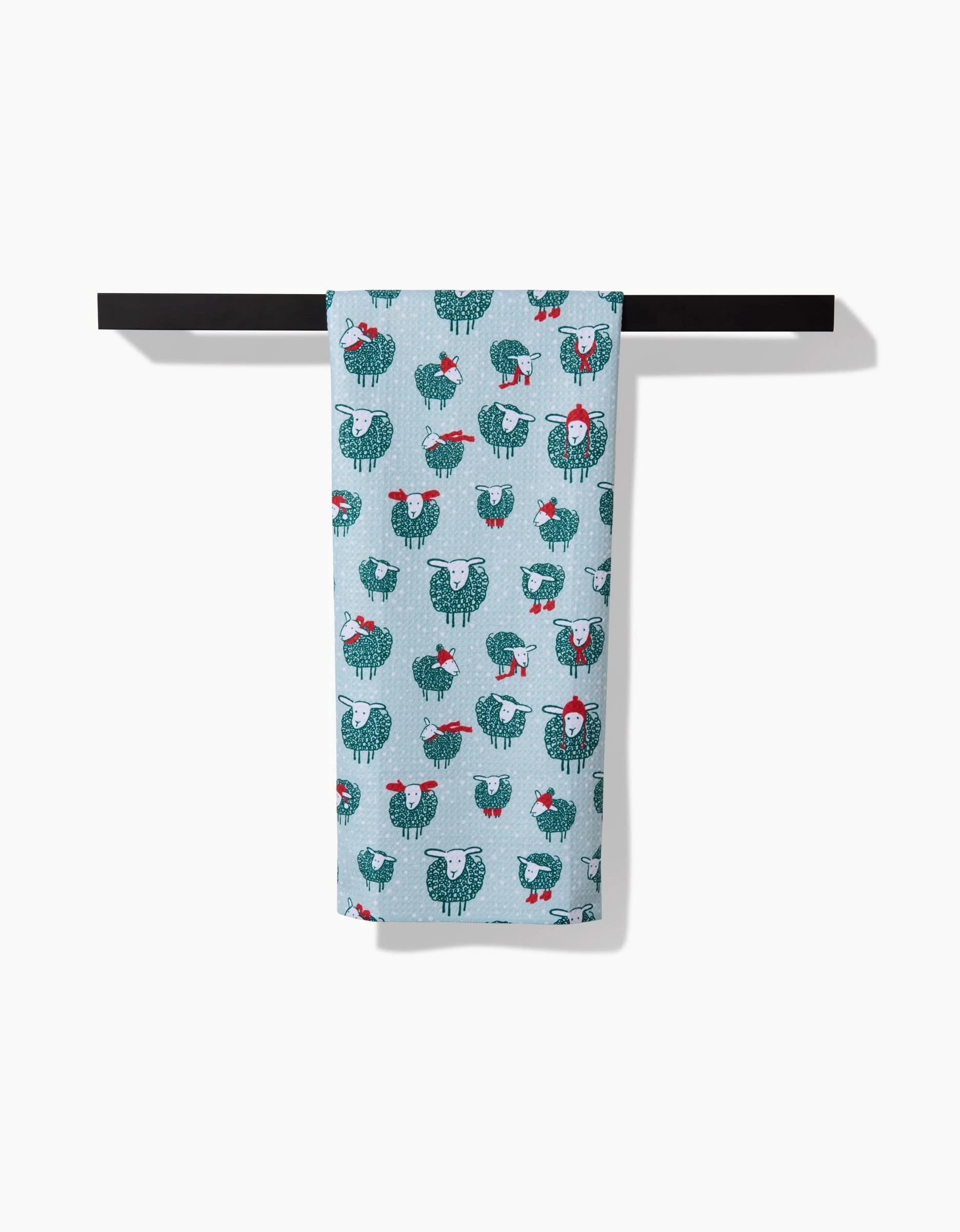 The Warm Woollysheep kitchen towel by Kris Ruff features a light blue color with teal and white chickens, red accents, and hangs neatly on a black bar against a white background.
