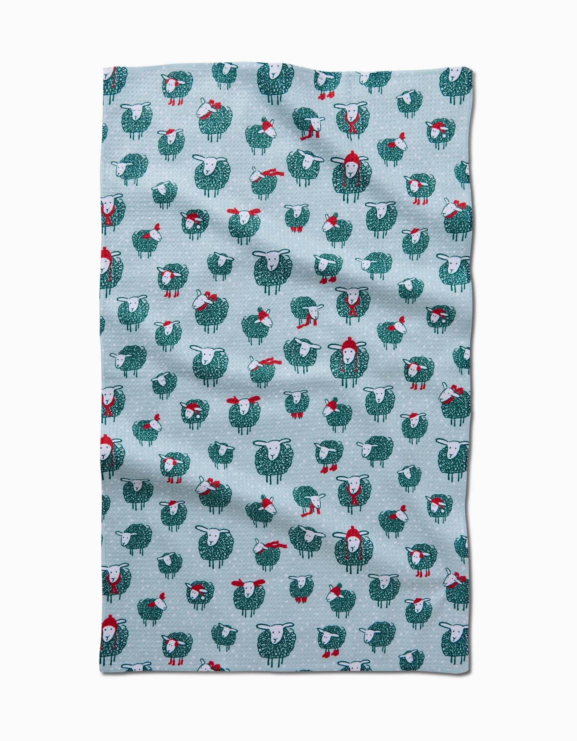 The Warm Woollysheep by Kris Ruff is a light blue, quick-drying towel with a slightly wrinkled texture and a repeating pattern of cartoon sheep in red scarves and Christmas wreaths.