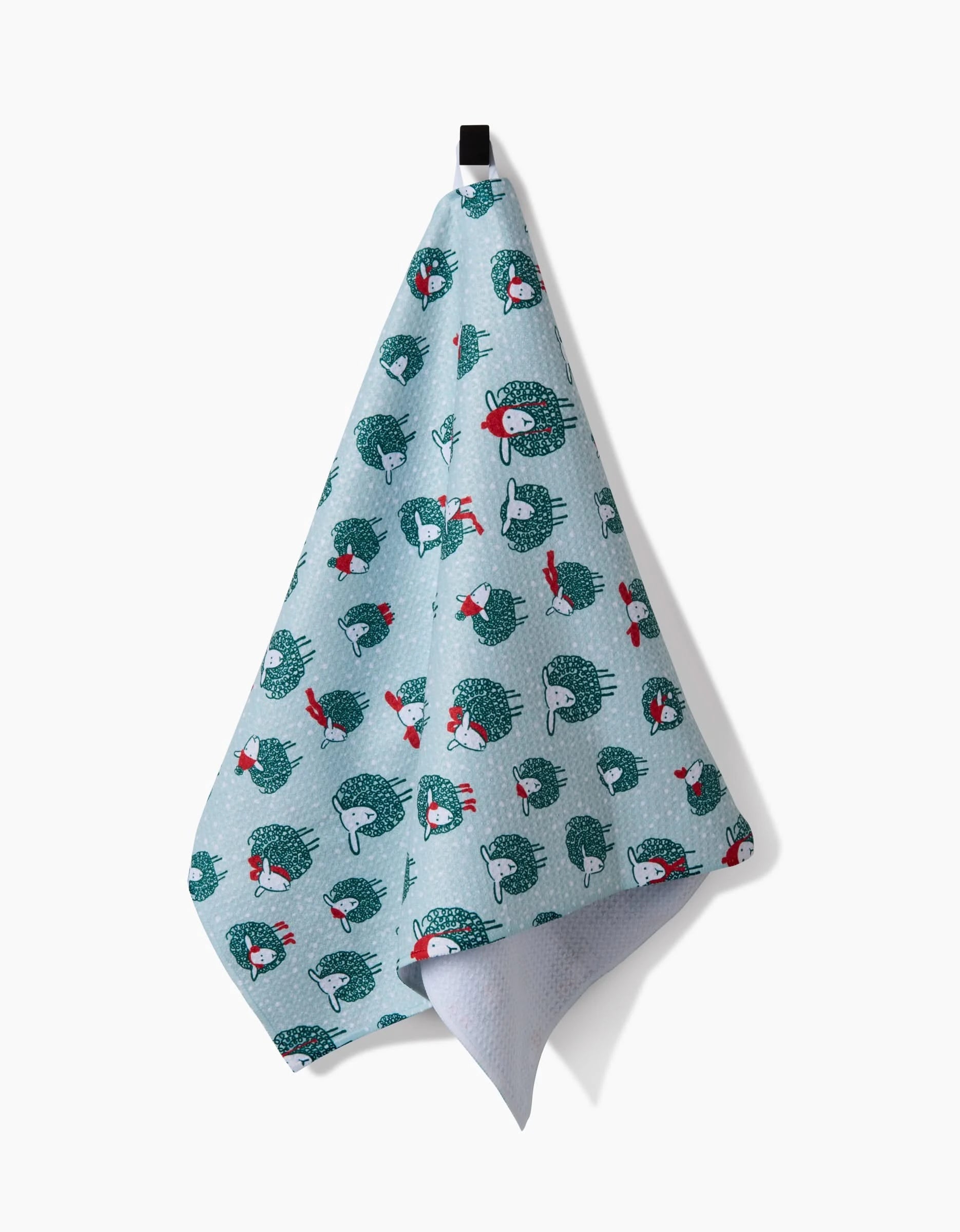 A Warm Woollysheep recycled kitchen towel by Kris Ruff, featuring light blue fabric with cartoon hedgehogs in red scarves and hats, hangs from a black hook against a white background.