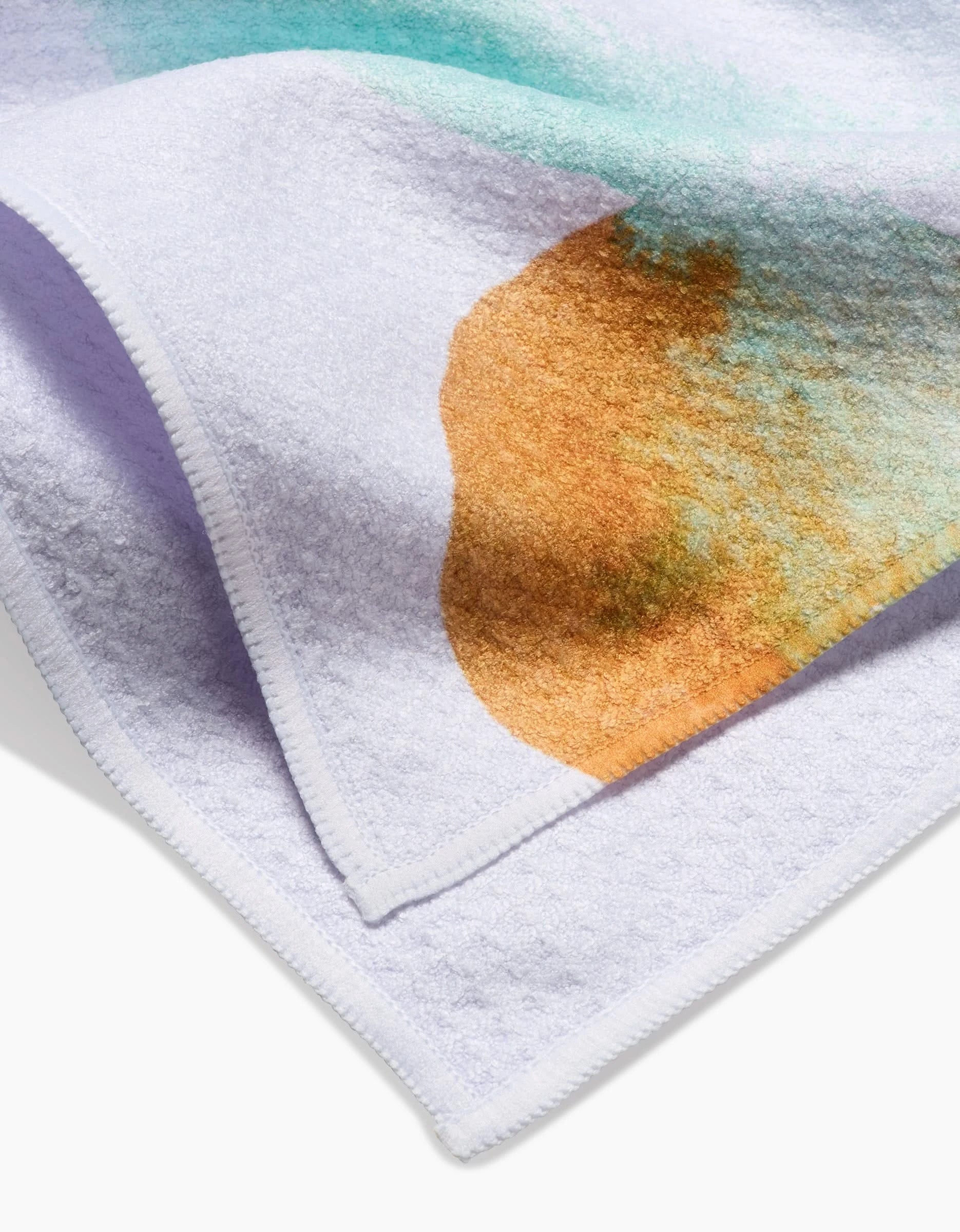 A close-up of the Taryn Brennan Watercolor Rocks tea towel features soft, textured Geoweave fabric with turquoise and orange watercolor patterns and neatly stitched edges.