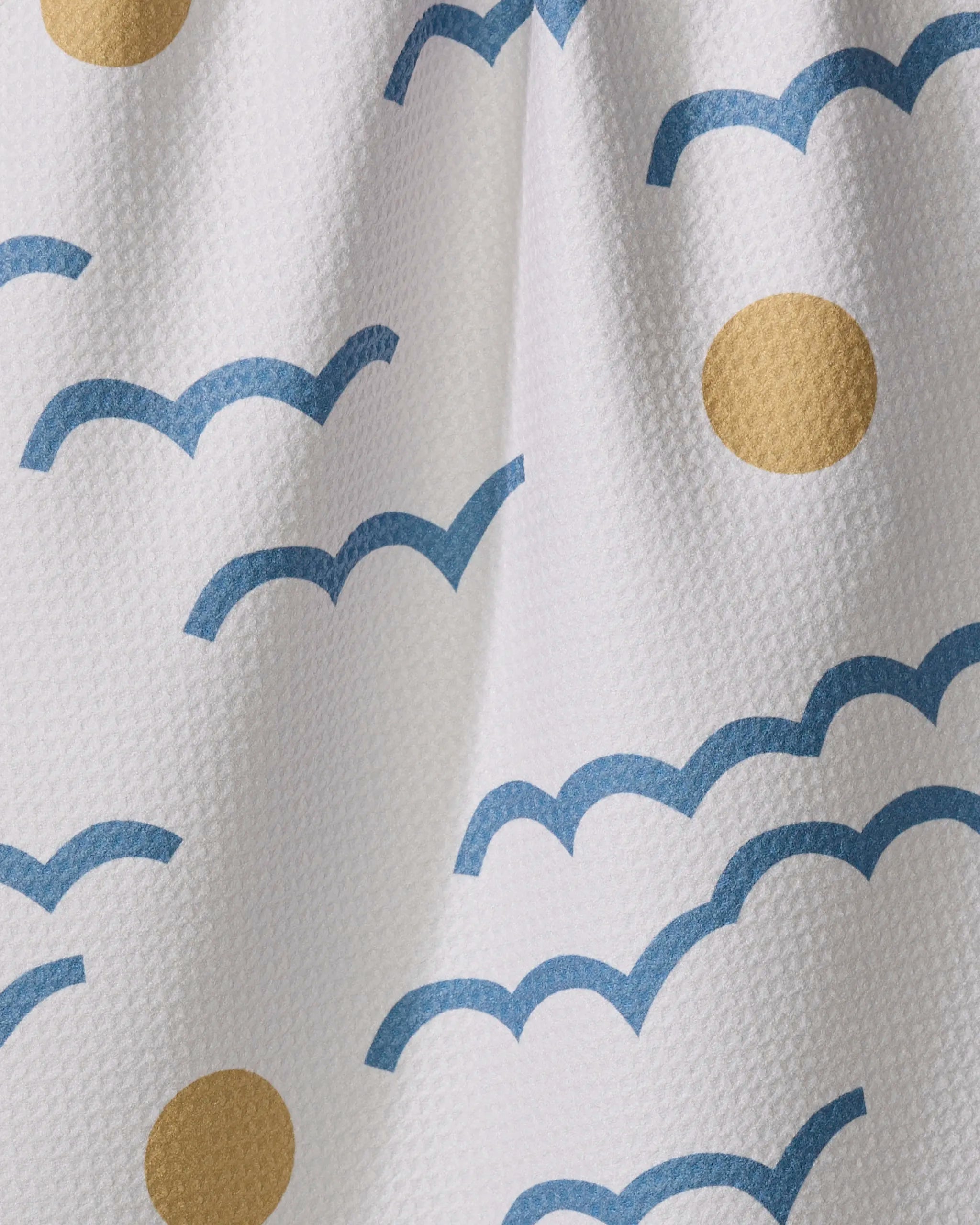The "Wavy Day" kitchen towel by Elizabeth Edwards is white and textured, featuring blue bird silhouettes and yellow circles for an eco-friendly design inspired by birds flying across a sunny sky.