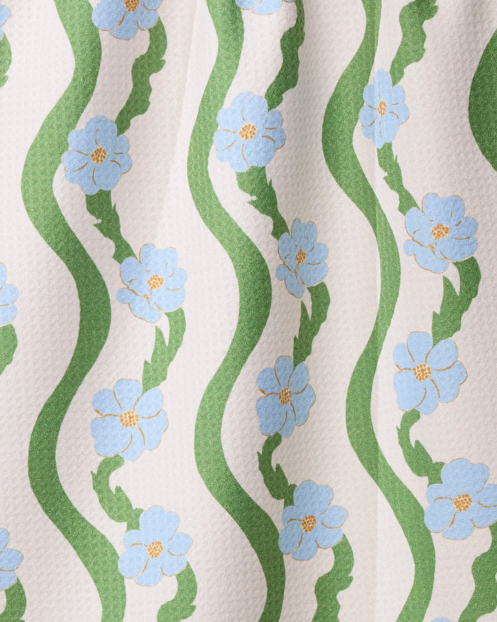 The Geometry "Wavy Flowers" tea towel features a wavy green stripe design with blue-and-yellow flowers on an off-white background, crafted from ultra-absorbent recycled materials.
