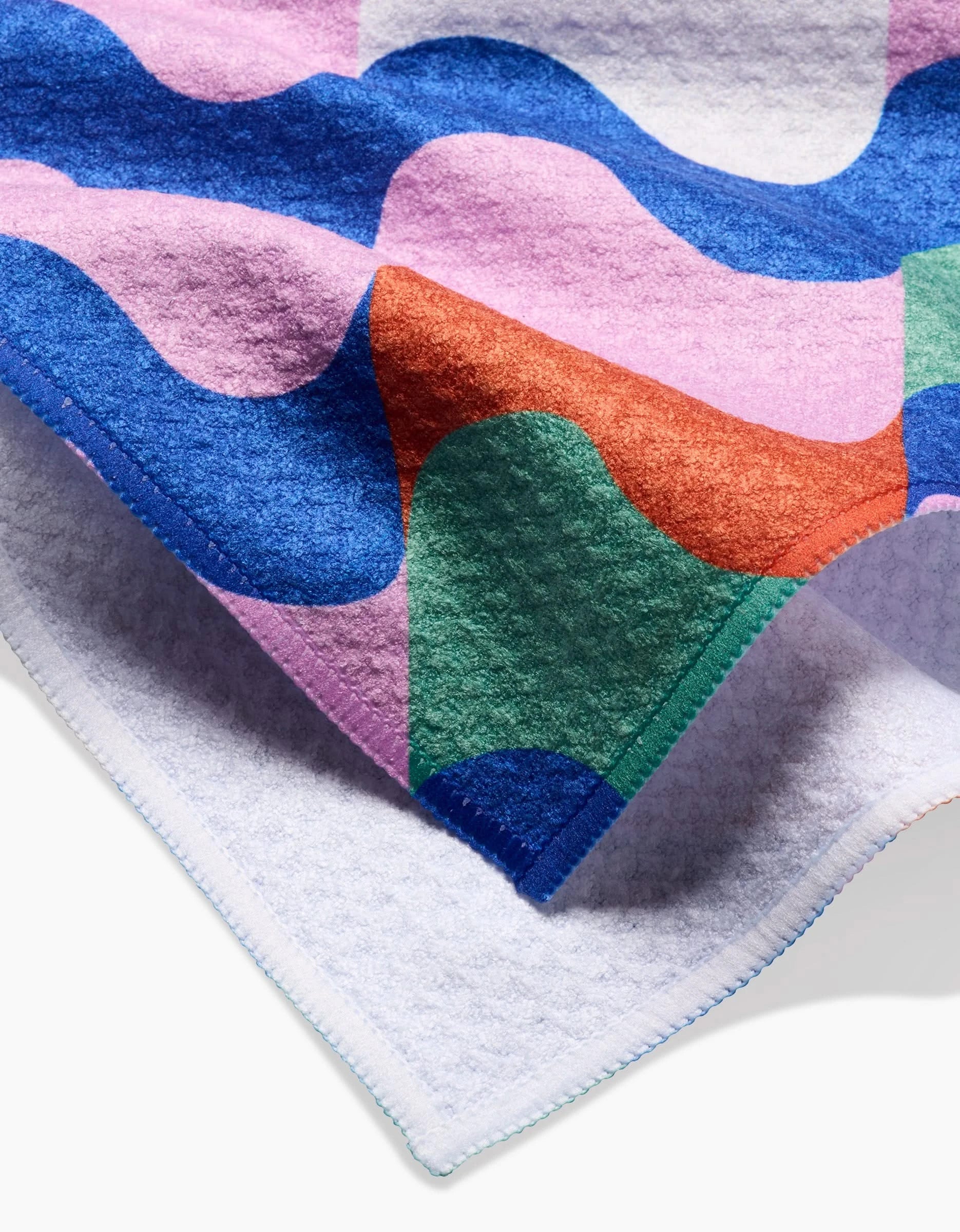 The Claire Iglesias Wavy Stripes blanket is made from recycled materials, featuring bold wavy patterns in blue, pink, green, and orange with stitched edging. Its abstract geometric design and plush texture make it cozy and eco-friendly.