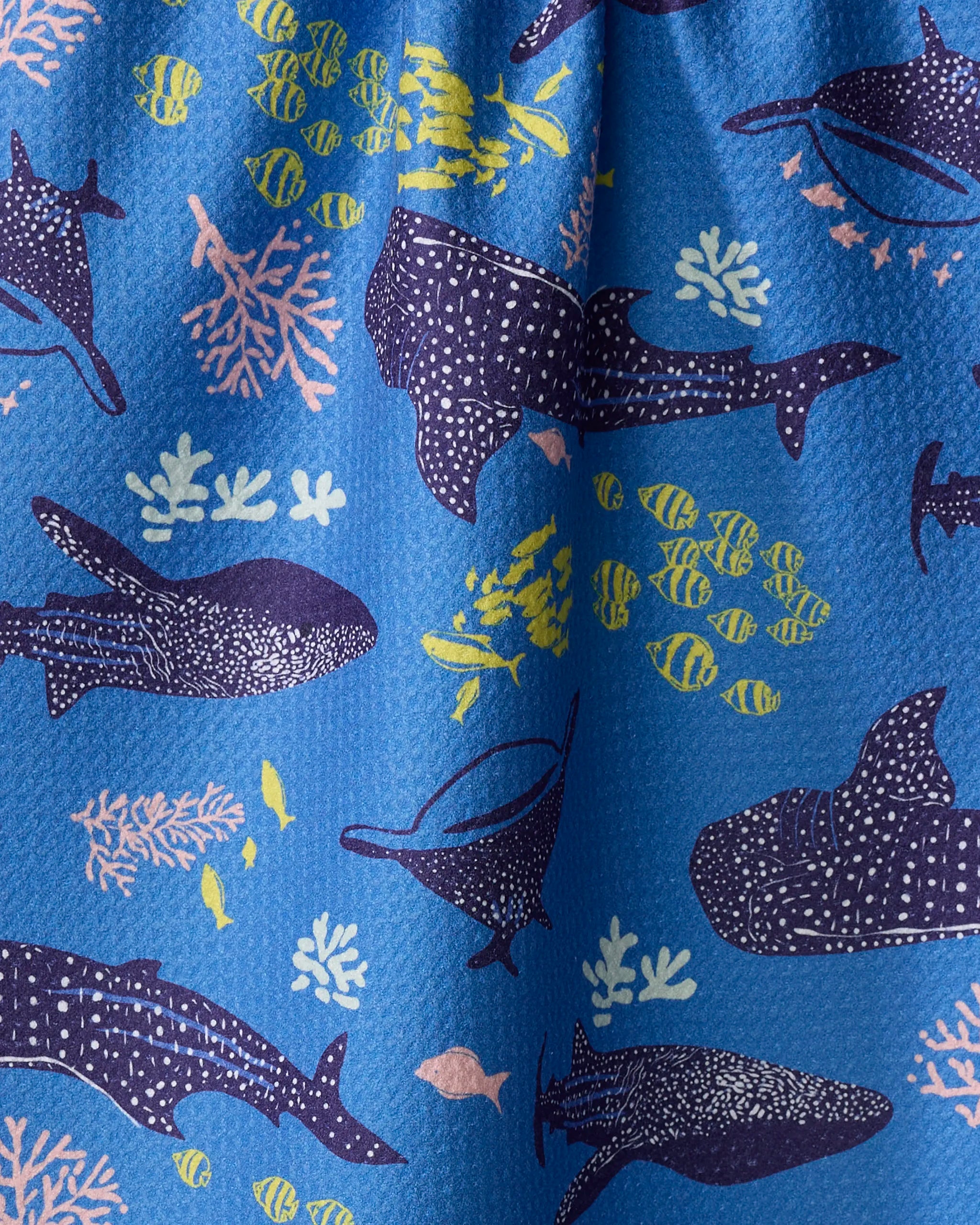 The Whale Shark dish towel by Elisabeth Wing features playful blue fabric with cartoon whale sharks, yellow fish, and pink coral. Absorbent and charming, it adds both style and practicality to your kitchen.