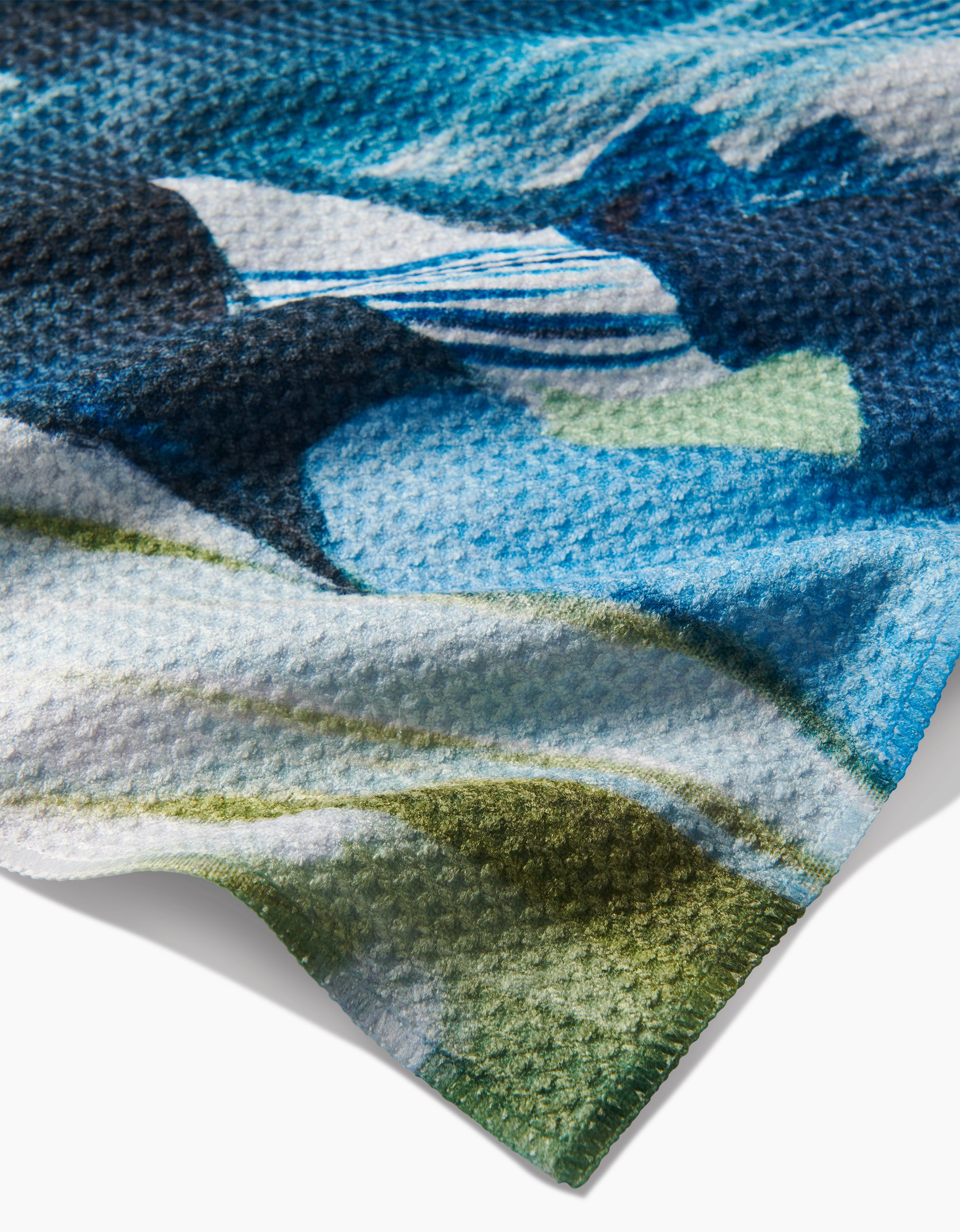 Close-up of the textured Geoweave fabric in Kelly Peters’ “Where He Laid To Go” tea towel, featuring a colorful abstract blue, green, white, and black pattern with a soft wavy edge—crafted from post-consumer recycled materials.