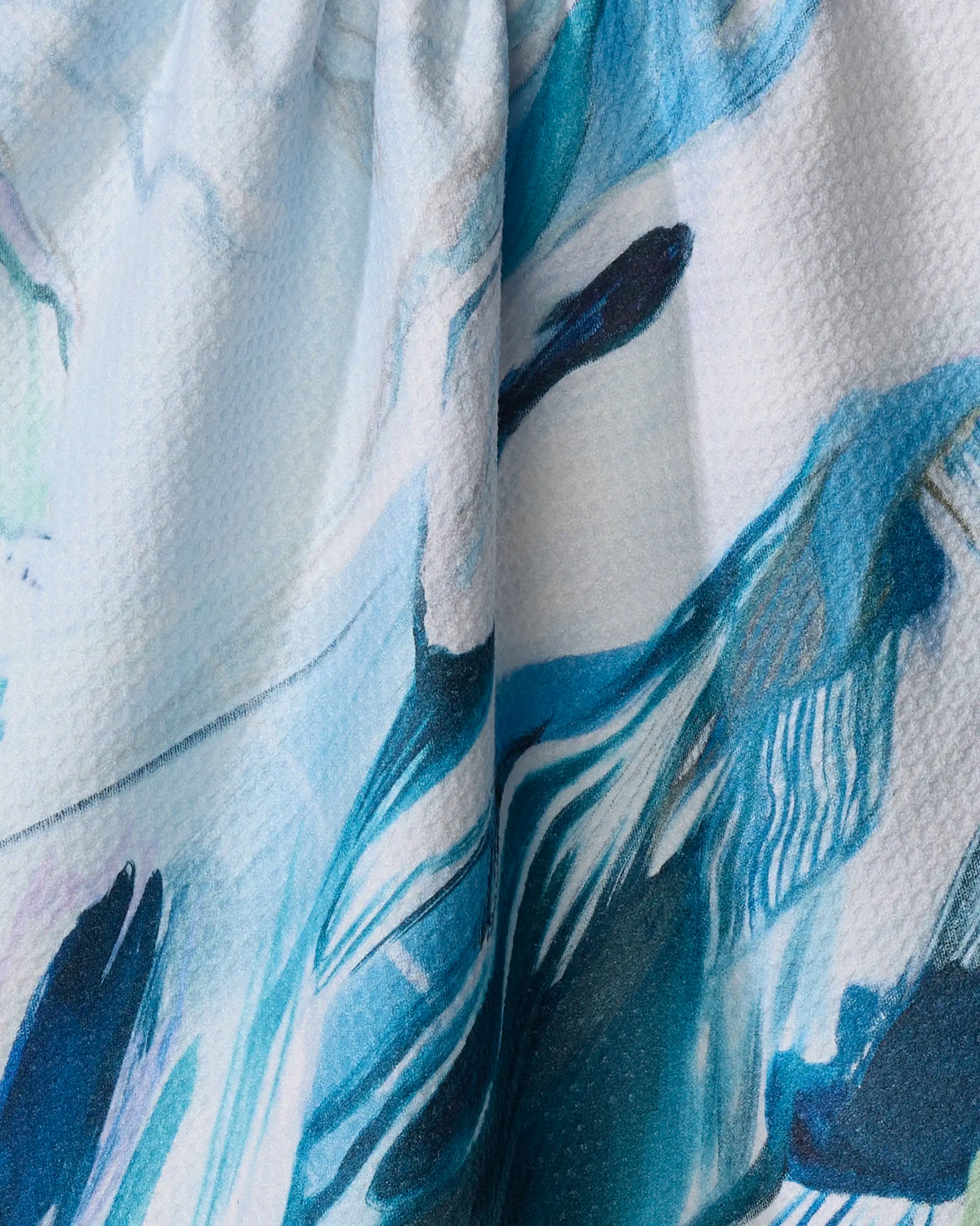 Close-up of "Where He Laid To Go" by Kelly Peters—a kitchen towel with a blue, teal, and white abstract pattern of brush-like strokes, crafted from recycled materials.