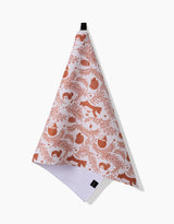 The Sara Mari Whimsical Woodland kitchen towel, featuring rust-orange bears, foxes, owls, and foliage on white ultra-absorbent fabric, hangs from a black loop against a plain white background.