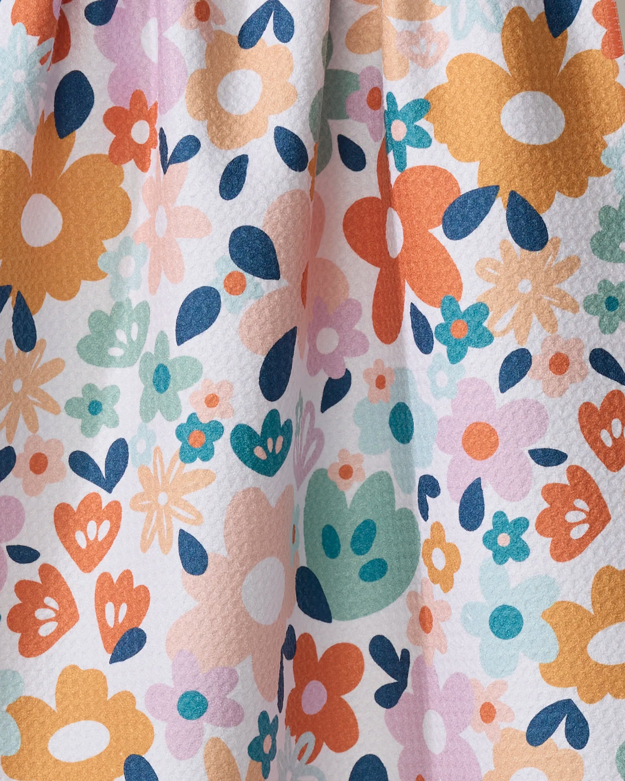 A close-up of Whimsy Floral fabric by Sara Mari, showcasing a colorful, textured floral pattern with orange, yellow, pink, blue, and green flowers on white—crafted from recycled materials for an eco-friendly touch.