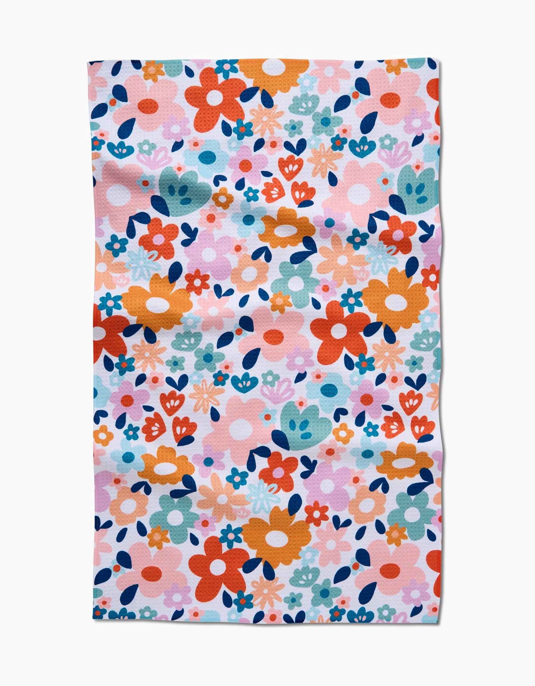 The Sara Mari Whimsy Floral is a rectangular cloth featuring orange, red, blue, pink, and teal flowers and leaves on white Geoweave fabric. The vibrant floral design adds charm to any setting.