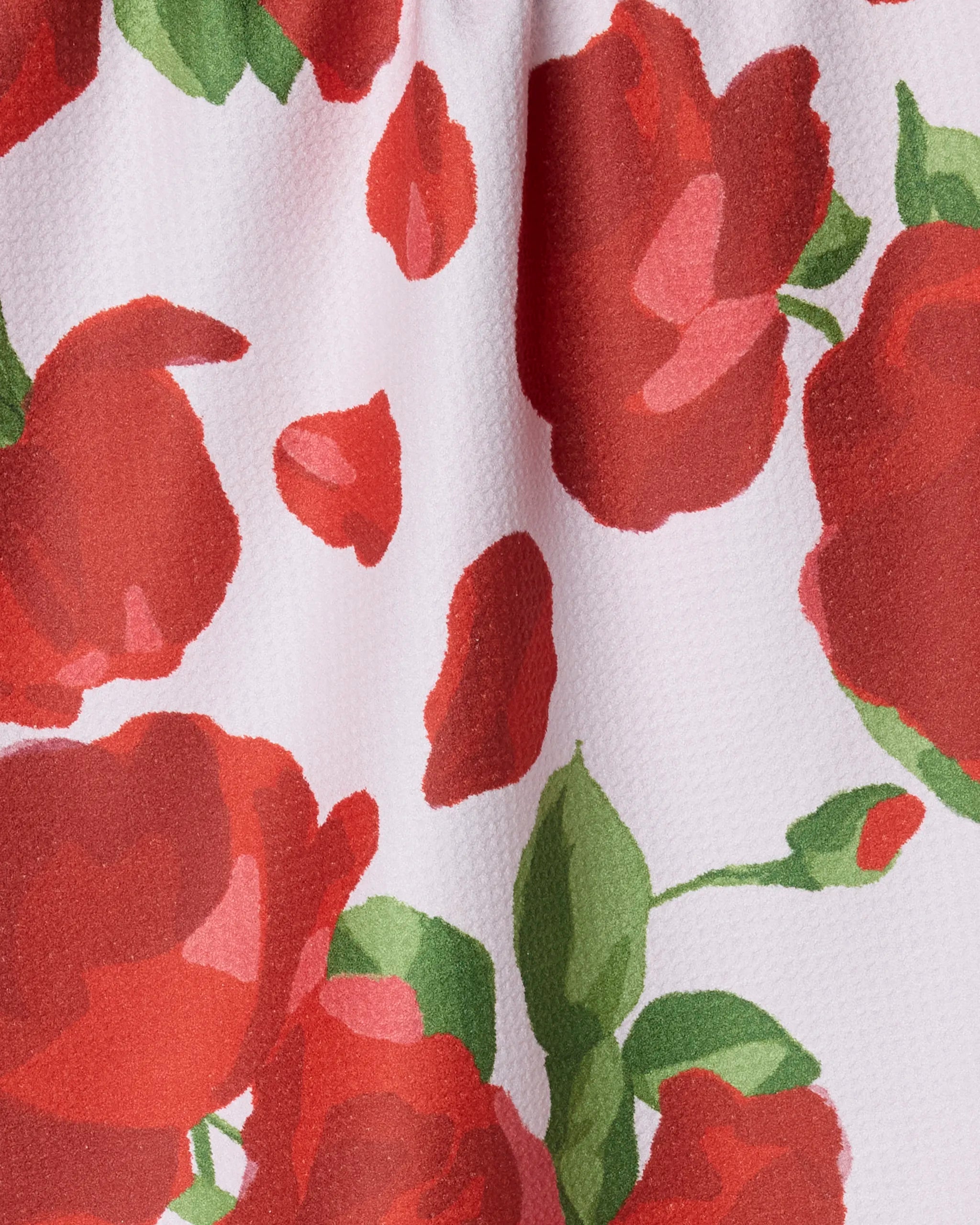 Close-up of Geometry's Whispering Roses tea towel, crafted from recycled materials with a soft texture. Features a vibrant floral design of bold red roses and green leaves on a crisp white background.