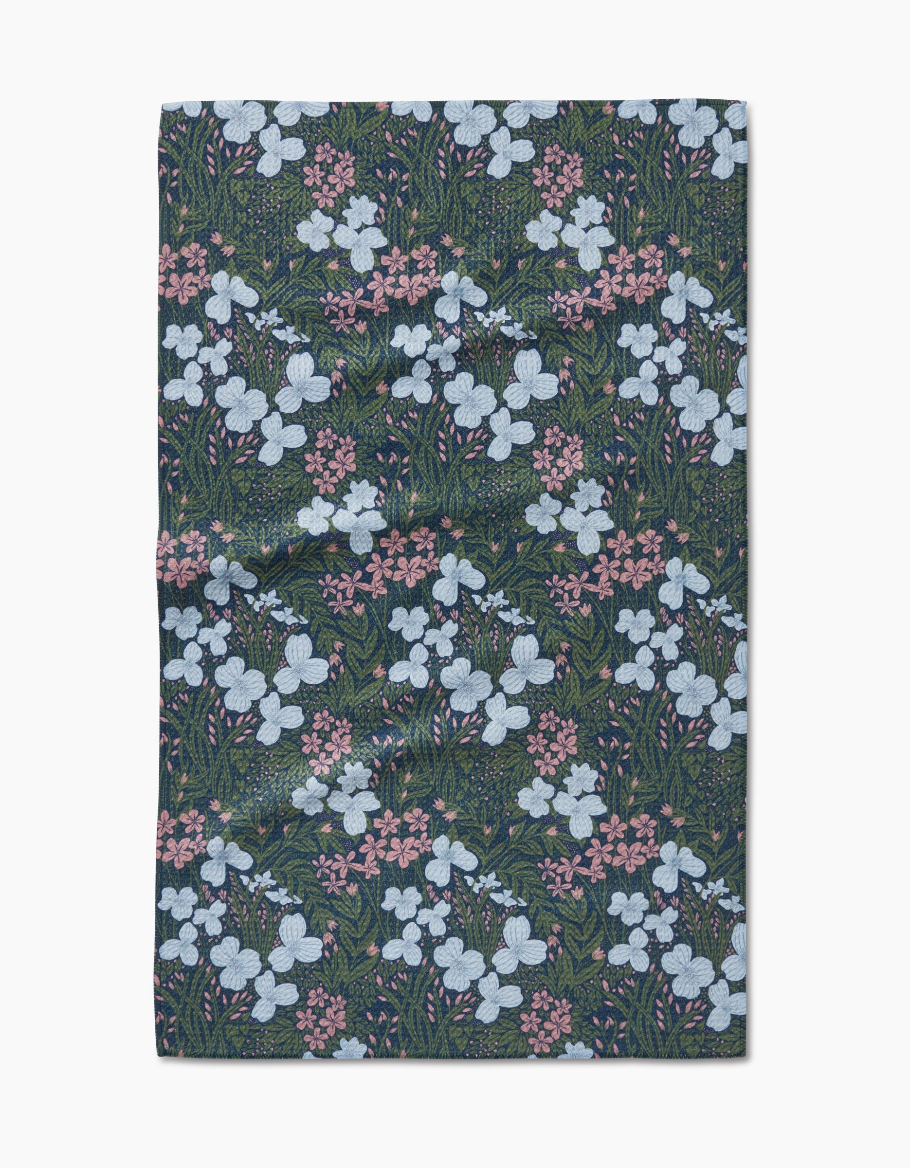 The White And Green Meadow Tea Towel by Katie OShea is crafted from Geoweave fabric and features a repeating pattern of white and pink flowers with green foliage on a dark background, shown flat on a white surface.