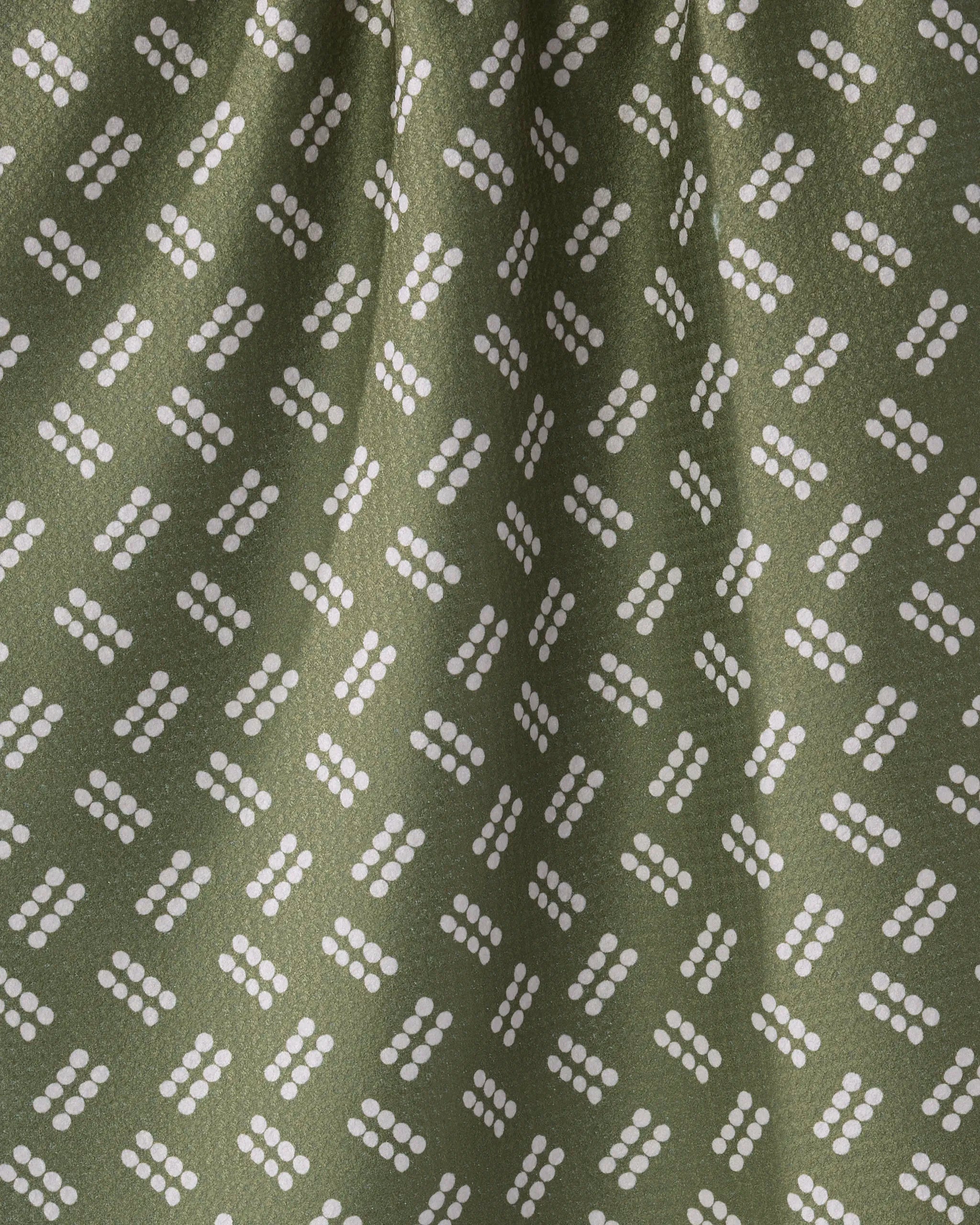 Wick by Geometry features an olive green fabric with diagonal white dots and geometric shapes, creating a modern, abstract look. Made from recycled materials, this fabric appears slightly gathered or draped.
