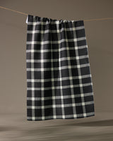The Geometry Wicklow Black kitchen towel, featuring a black and white checkered pattern, hangs on a clothesline against a simple, neutral background.