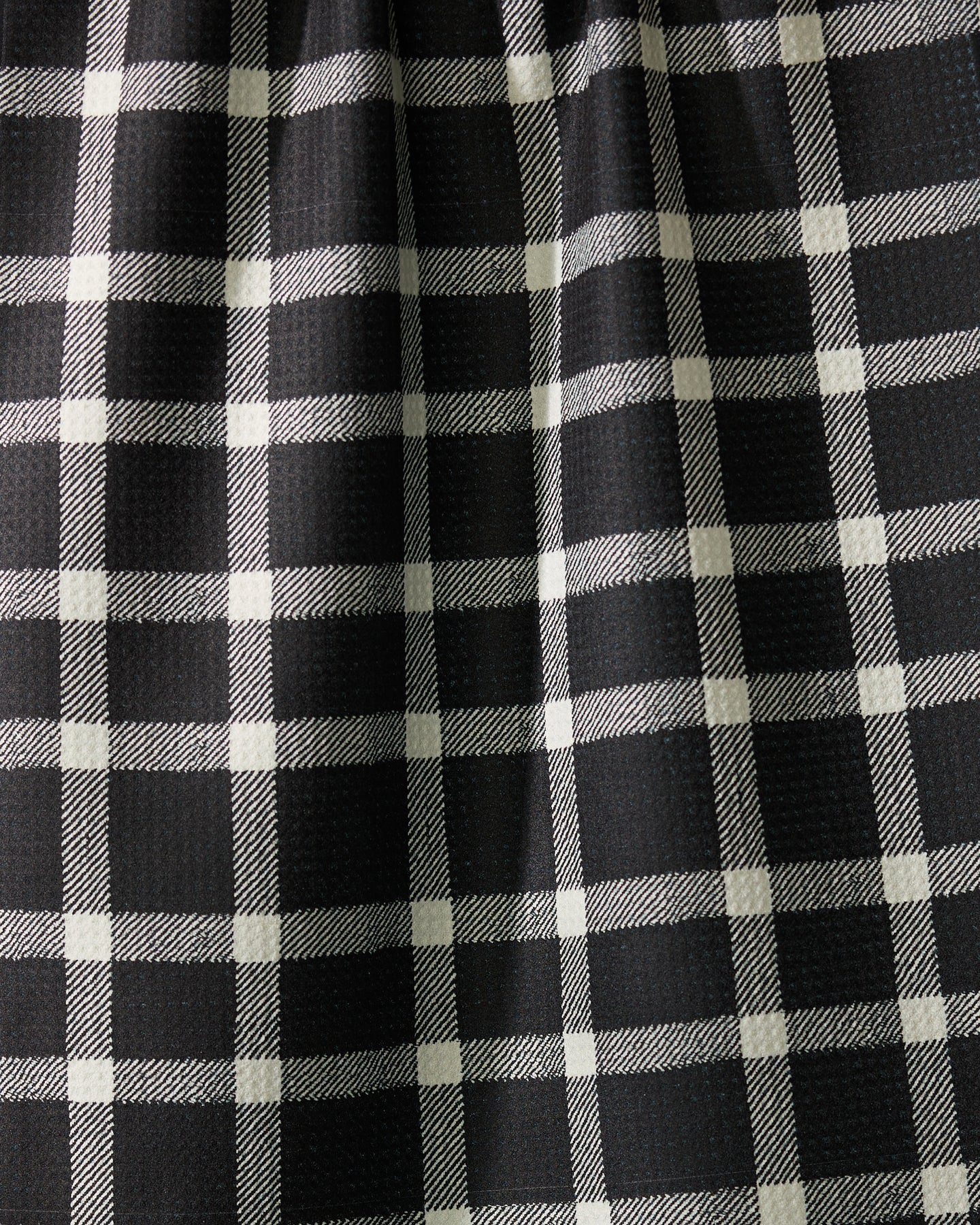 Close-up of Geometrys Wicklow Black: black fabric with a white plaid pattern, slightly gathered to form gentle vertical folds and subtle shadows across the grid design.
