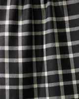 Close-up of Geometrys Wicklow Black: black fabric with a white plaid pattern, slightly gathered to form gentle vertical folds and subtle shadows across the grid design.