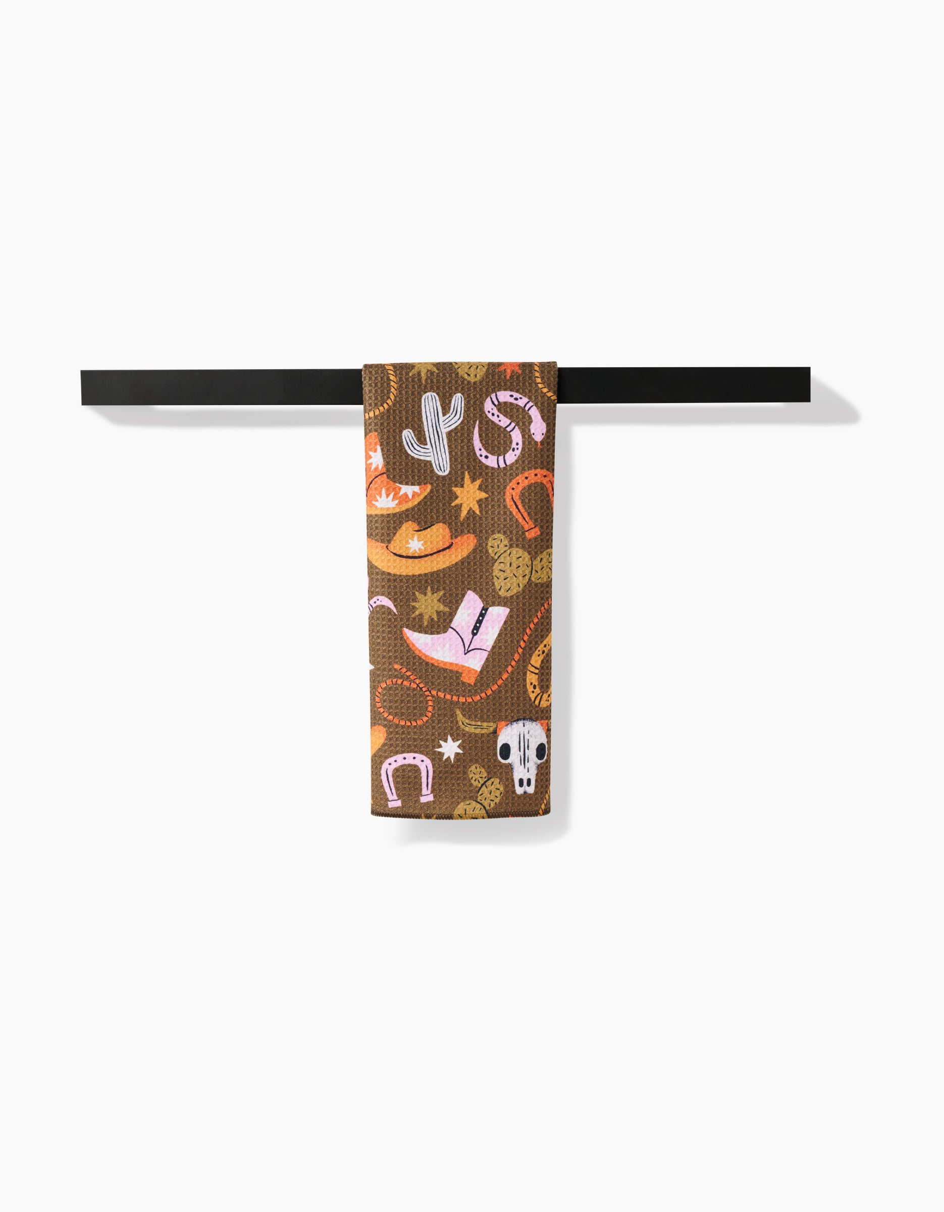 The Megan Roy Wild Cowboy towel, crafted from ultra-absorbent Geoweave and featuring vibrant cowboy-themed prints, hangs neatly on a black towel bar against a white background.