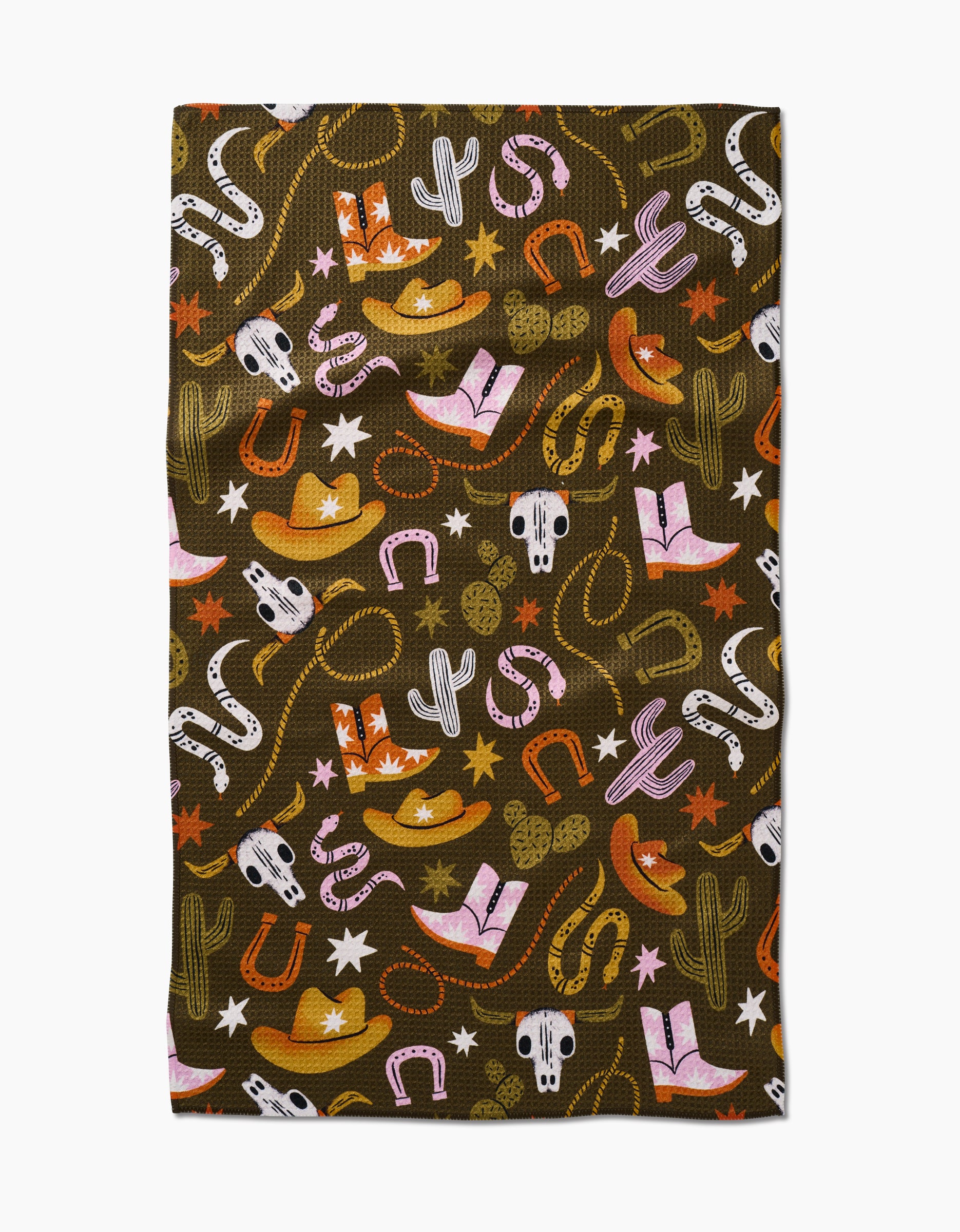 The Wild Cowboy by Megan Roy is made from ultra-absorbent Geoweave fabric and features a western-themed print with cowboy hats, boots, cacti, horseshoes, skulls, stars, lassos, and snakes in orange, pink, white, and green on dark brown.