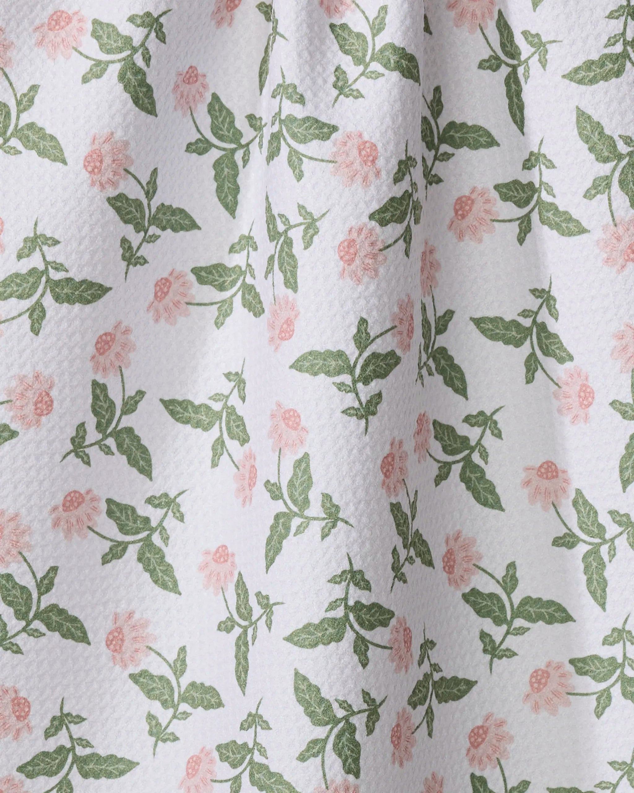 The Danelys Sidron Wildflower Vine Blush tea towel features a white textured surface with green leaves and pink flowers in a repeating pattern. Creases and folds add to its ultra-absorbent, soft, and natural look.