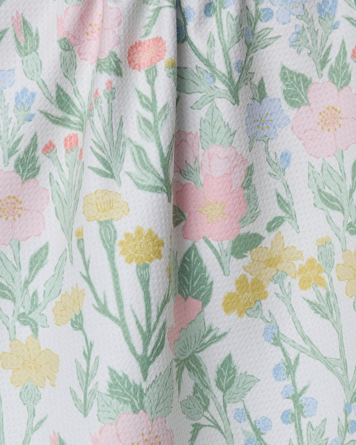 A close-up of the Wildflowers in Bloom kitchen towel by Jasmine Blooms Designs, made from recycled materials with a textured white fabric featuring pastel pink, yellow, and blue flowers with green leaves.