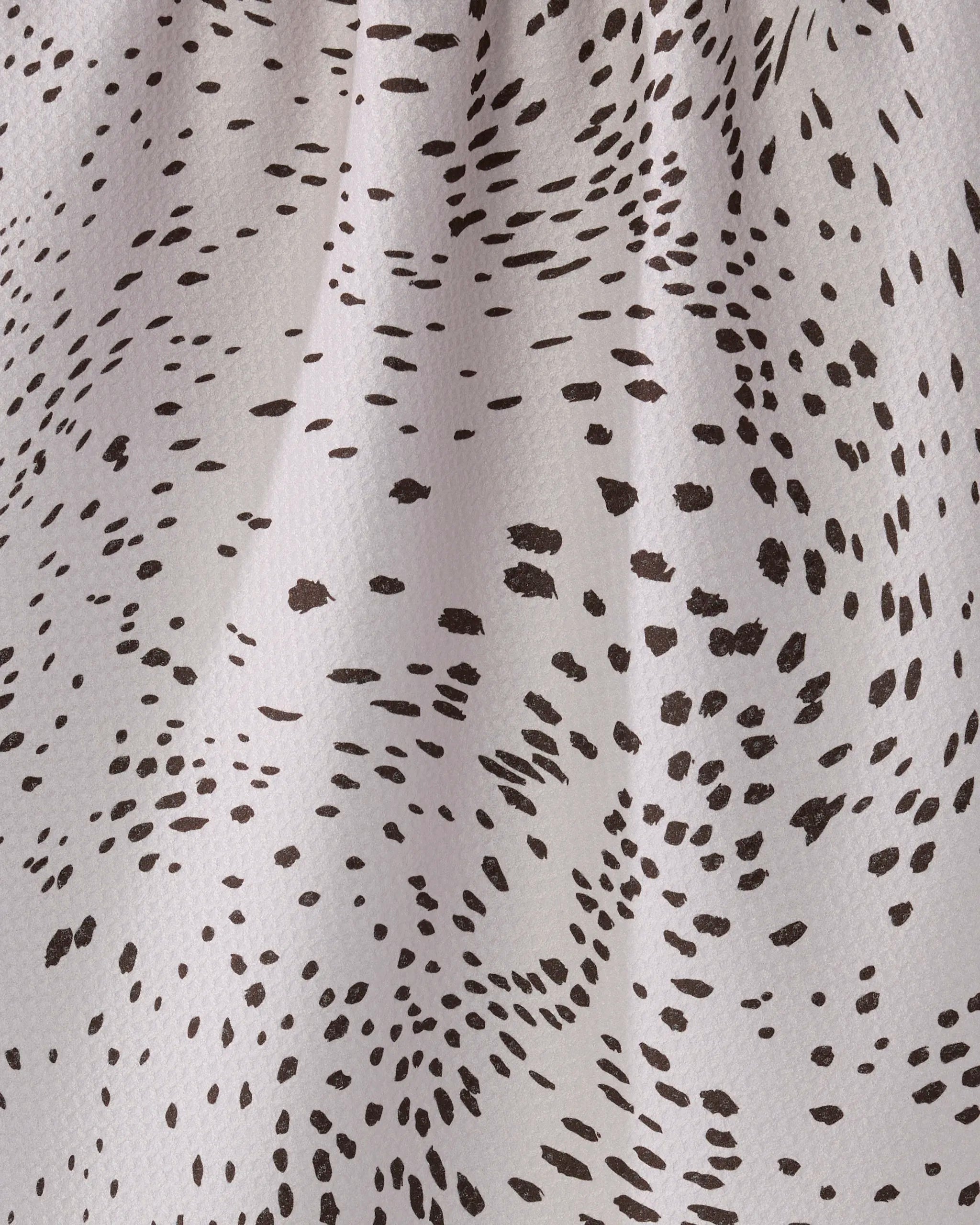 Close-up of the Wildgrain kitchen towel by Geometry, showcasing eco-friendly white fabric with irregular black dots in swirling clusters. The dynamic, abstract design is highlighted by subtle texture and folds.