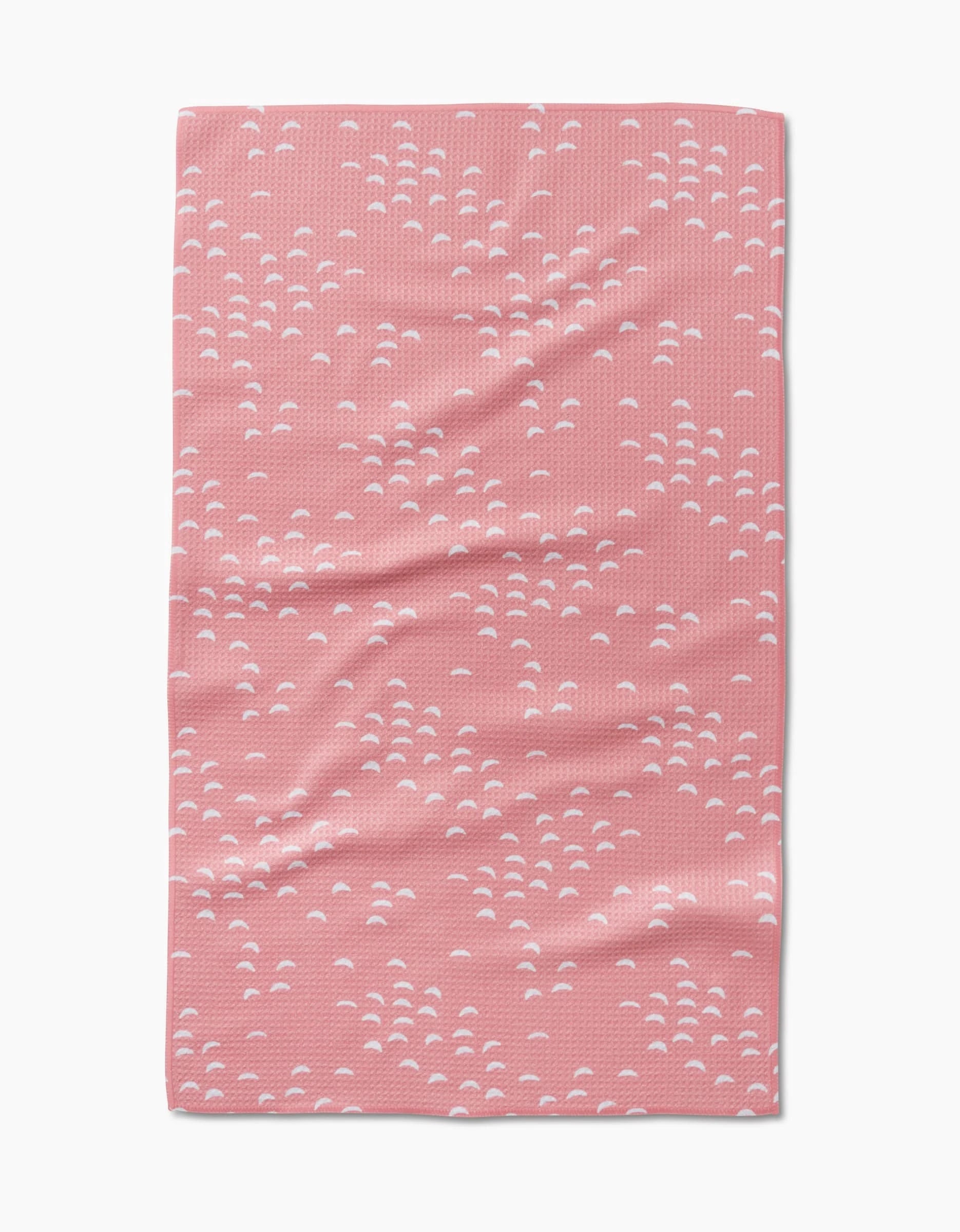 The Windswept kitchen tea towel by Jessica Swift features a repeating pattern of small white semi-circular clusters on pink. Made from recycled materials, it looks soft with gentle folds and creases throughout.