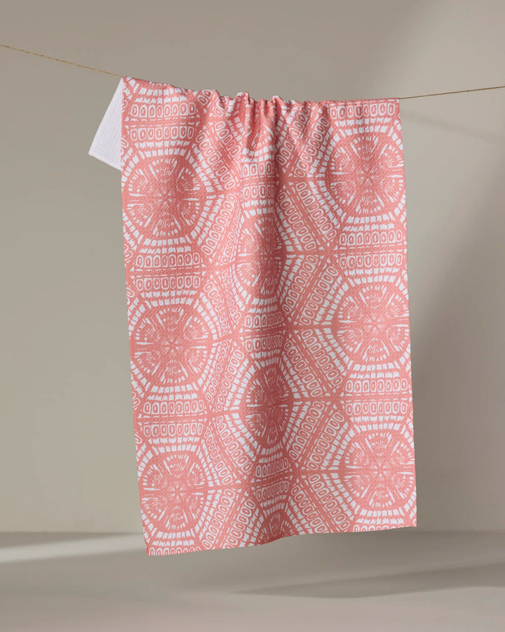 The Wings tea towel by Renee Fly, crafted from recycled materials, features pink and white circular geometric patterns and hangs on a line against a neutral background.