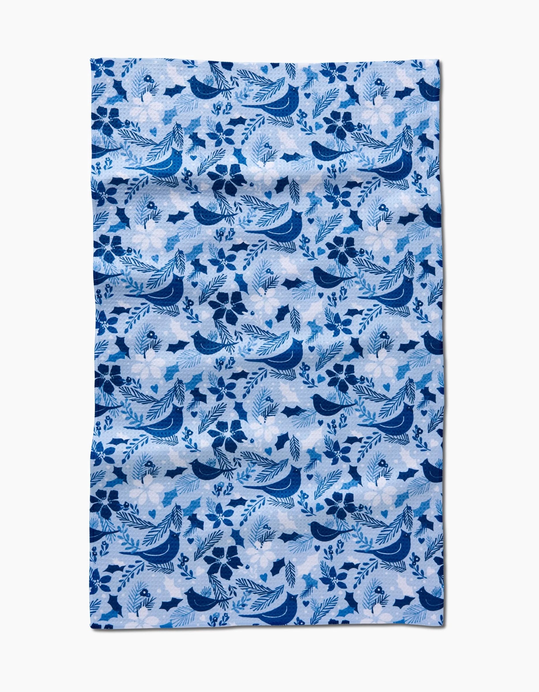 The Winter Birds tea towel by Kris Ruff features a blue and white floral and bird pattern on light blue, with ultra-absorbent fabric displaying repeating flowers, leaves, and birds in a decorative motif.