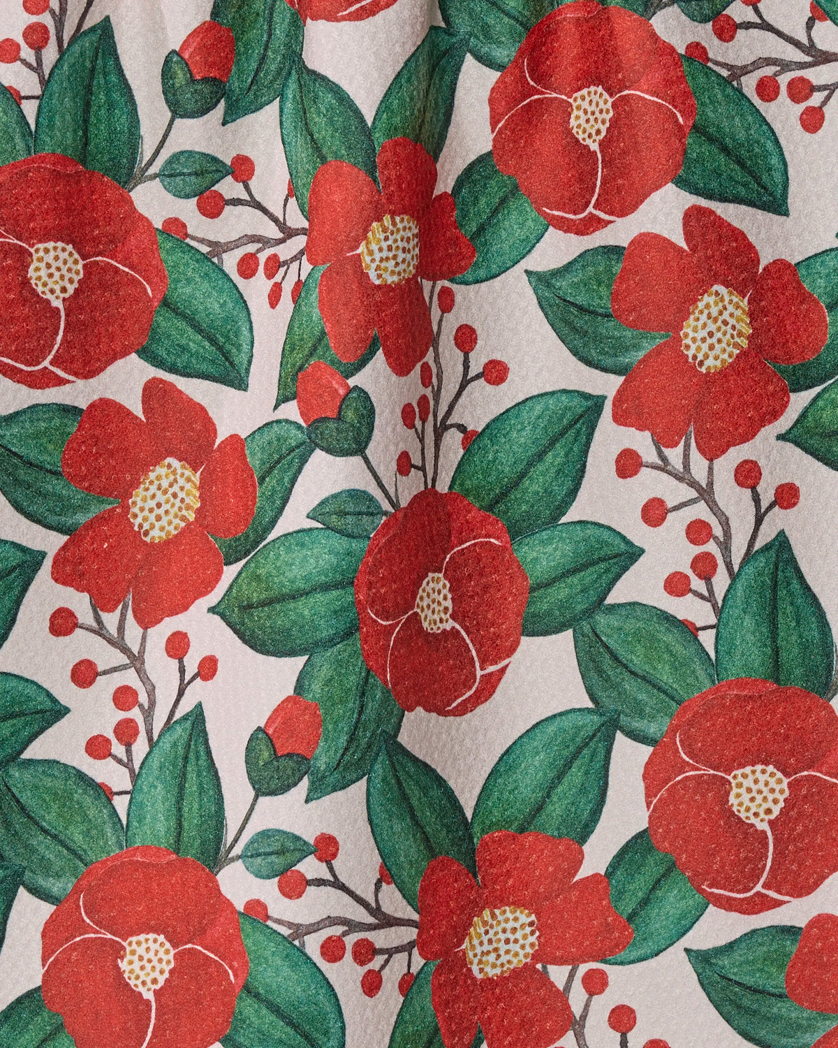 The “Winter Camellia” tea towel by Geometry features a patterned fabric with red flowers with yellow centers, green leaves, and small red berries on a light background. The repeating floral design creates a cheerful, botanical look—perfect for brightening up your kitchen, and it’s thoughtfully made from recycled materials.
