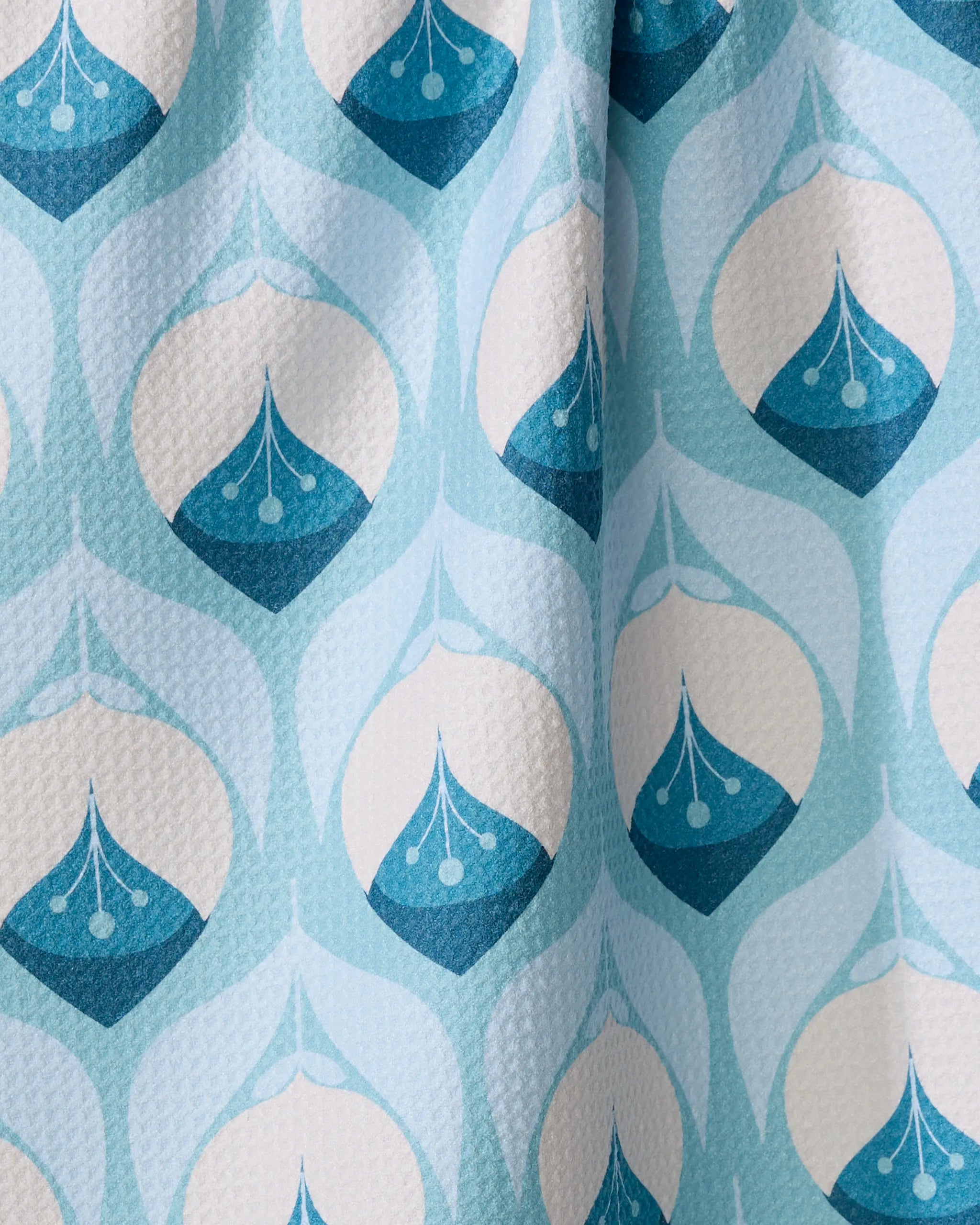 The "Winter Florals" kitchen towel by Blissful Flamingo features a light blue and white geometric teardrop pattern. Gentle folds add texture, making this recycled tea towel both stylish and eco-friendly.