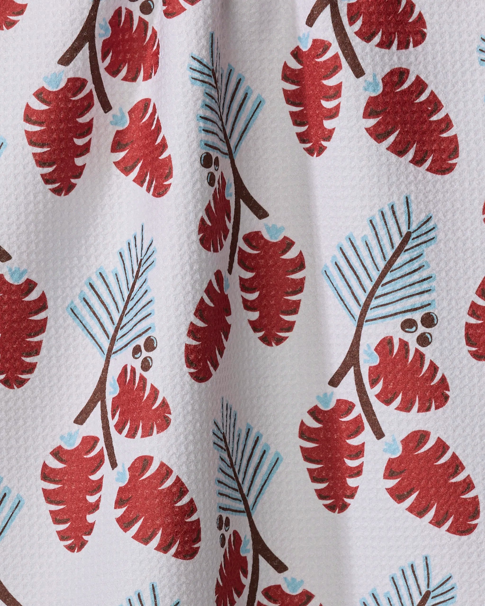 The "Winter Forage" kitchen tea towel by Lizzie Clark features a white fabric with red pinecones, brown branches, and blue pine needles. Made from recycled materials, its slight wrinkles add texture and charm to your space.