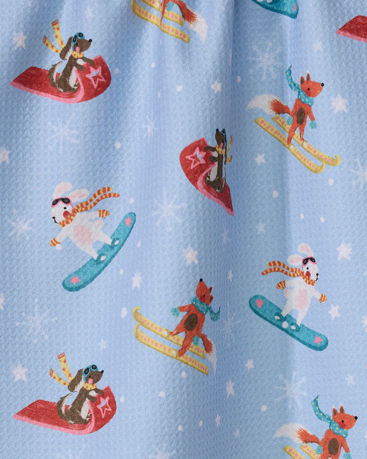 Winter Friends by Geometry features foxes and dogs in scarves and goggles, snowboarding and sledding amid snowflakes—a fun, eco-friendly tea towel for your kitchen.