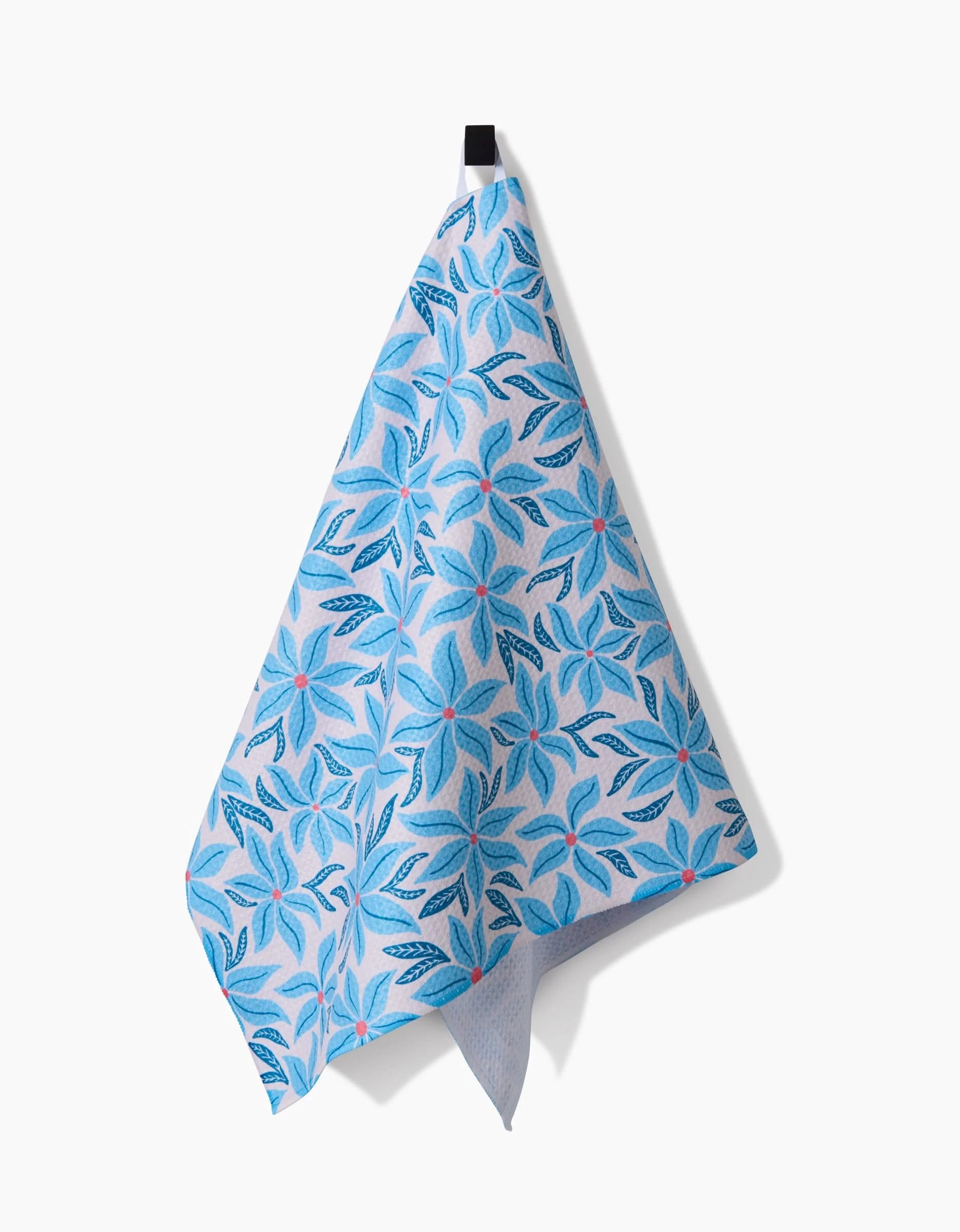 The Kayla Ann Winter Poinsettia tea towel, featuring ultra-absorbent fabric and a floral design with blue leaves and red dots, hangs from a black hook against a plain white background.