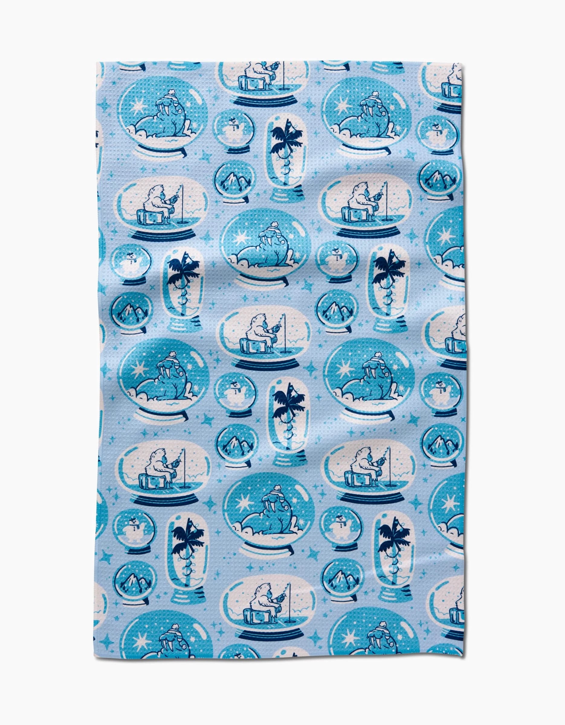 The Carly Berry Winter Snow Globe Collection tea towel features blue and white polar bear snow globe patterns with snowflakes and stars on a light blue background, made from ultra-absorbent recycled materials.