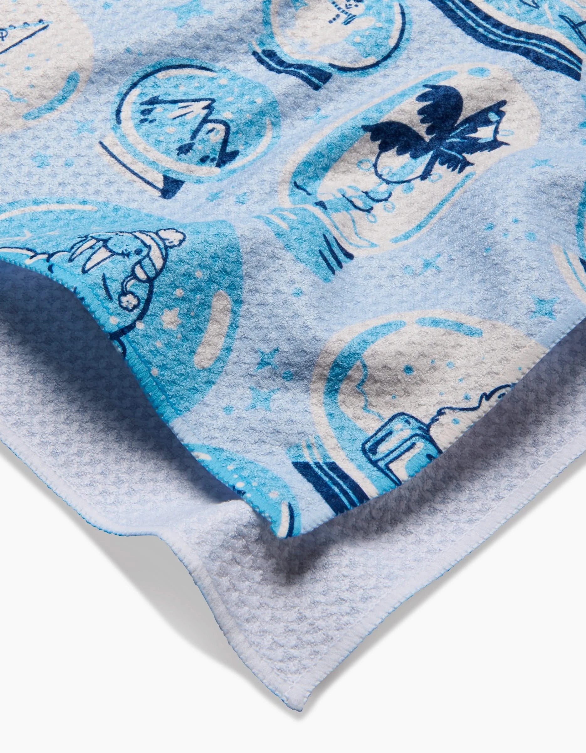 A close-up of Carly Berry’s Winter Snow Globe Collection tea towel in light blue, featuring playful snow globe and snowman illustrations in blue tones with a textured edge.