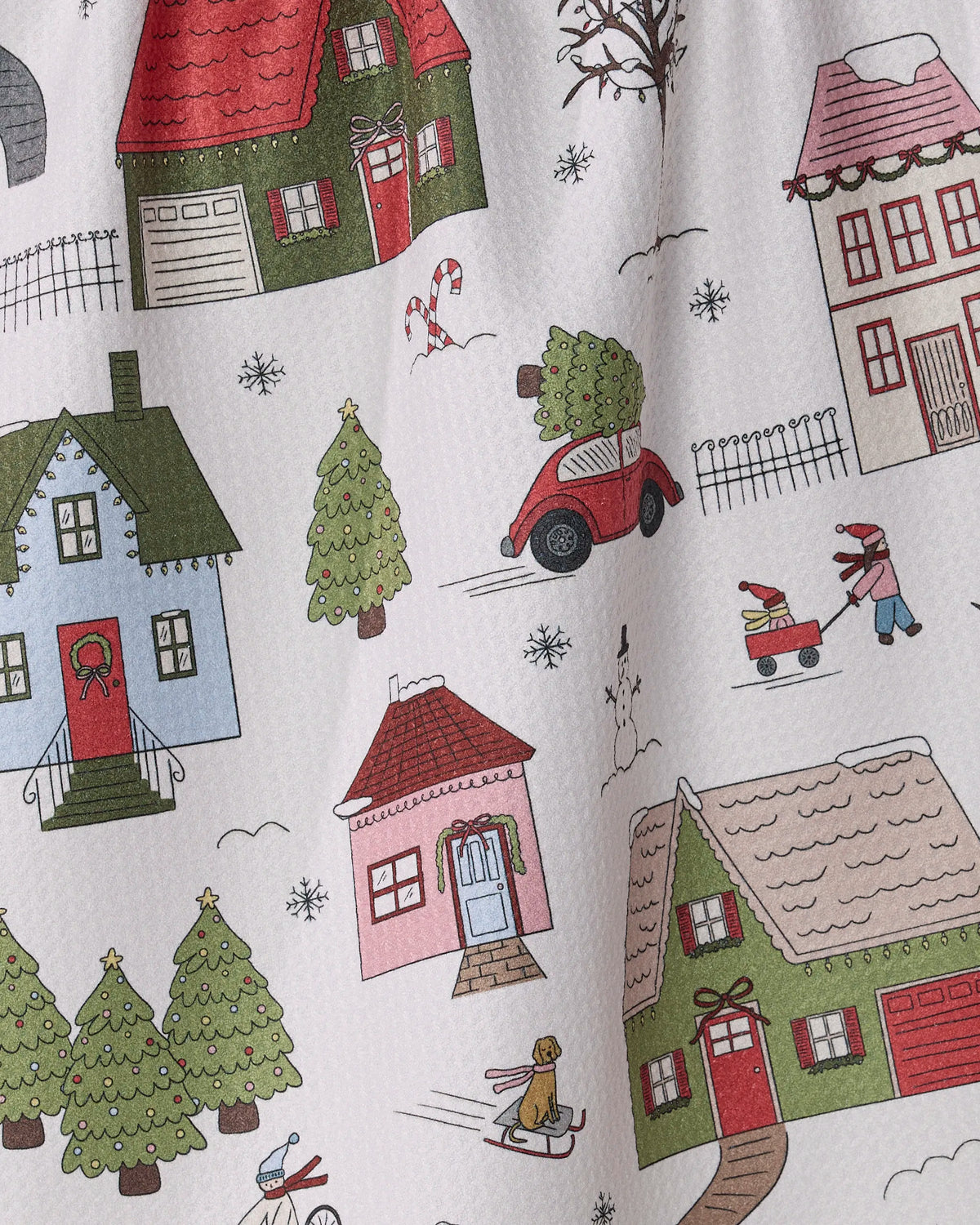 Add festive flair to your kitchen with Geometry’s “Winter Village” tea towel—featuring a vibrant illustration of colorful houses, cars, trees, and bundled-up people amid snowflakes and holiday decorations on a white background. Made from recycled materials for a cheerful, eco-friendly touch.