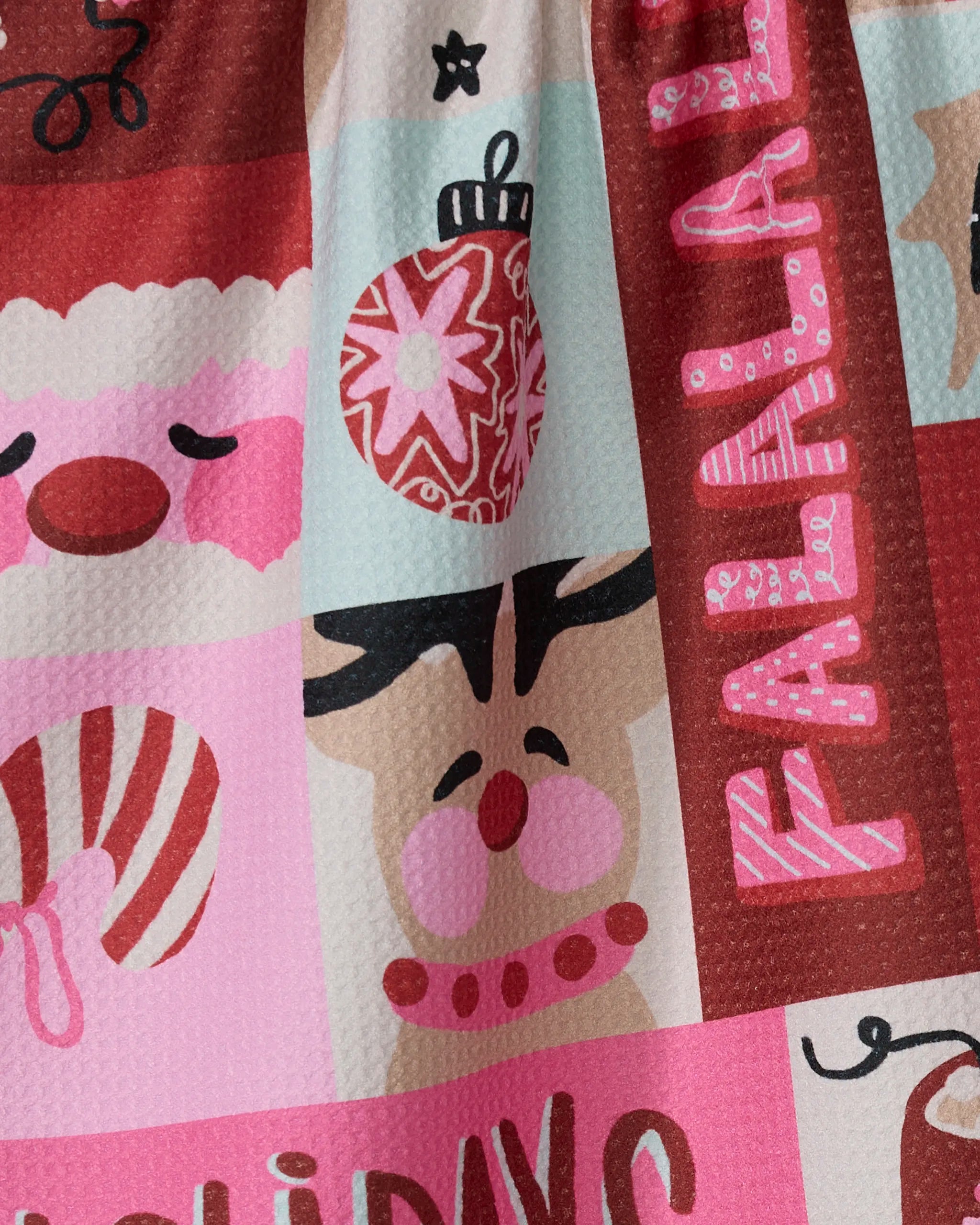 The Winter Wonder kitchen towel by Geometry features festive cartoon faces—Santa, reindeer, ornament, candy cane—and bold pink "FALALA" lettering in red, pink, and mint, perfect for bringing holiday cheer to your kitchen.